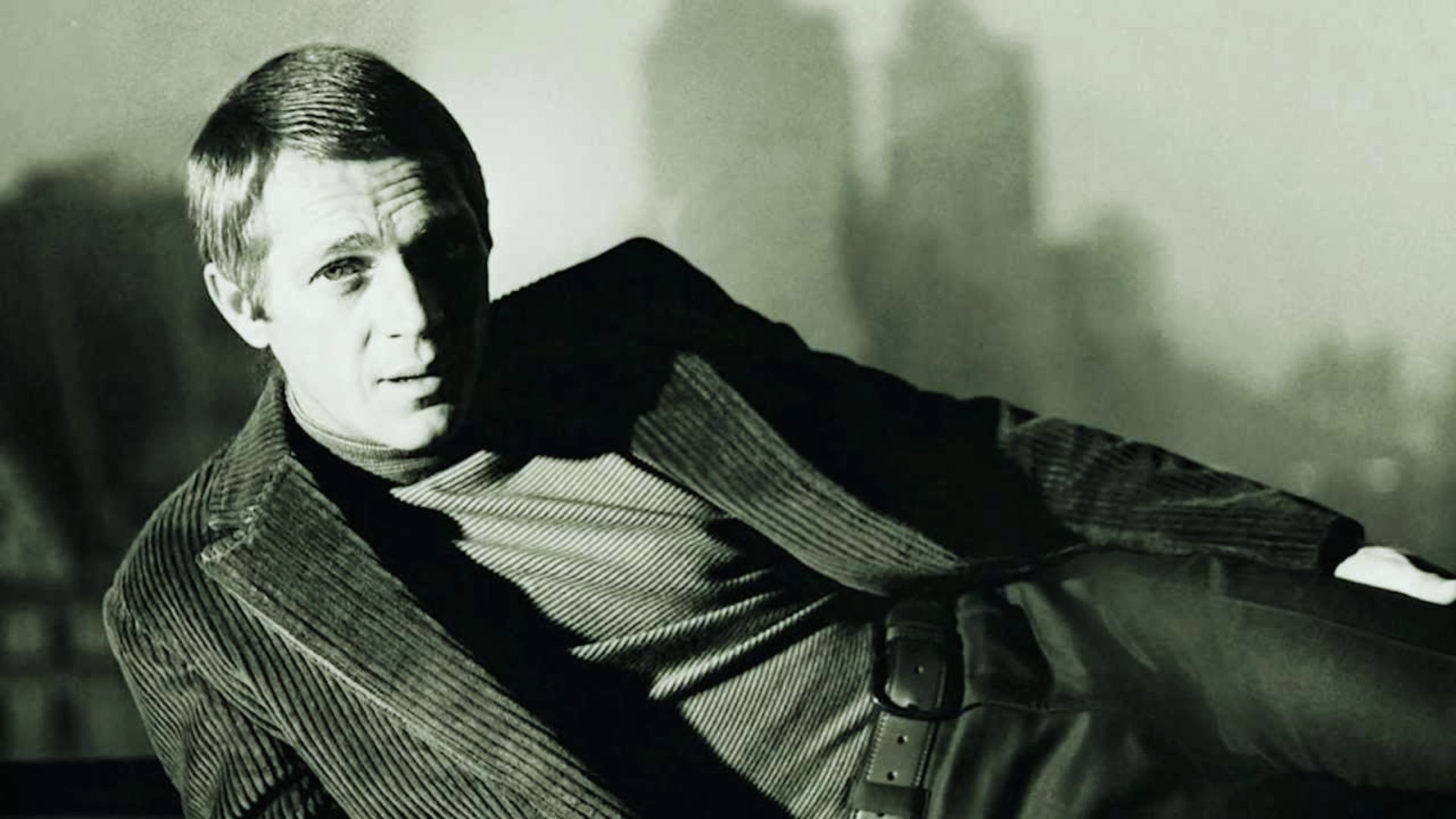 "A man in a suit sits on a bench, looking thoughtfully into the distance."