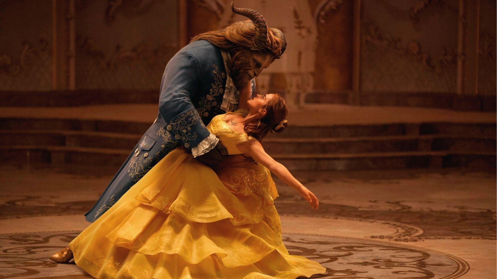 Belle in a yellow ball gown dancing with Beast in a blue coat in the ballroom.