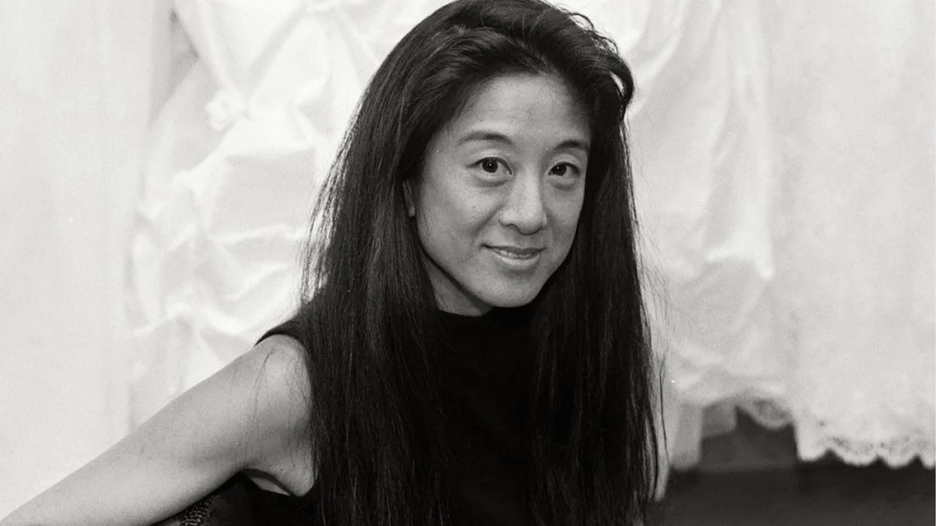 Black and white portrait of smiling woman with long hair in sleeveless black top against dresses