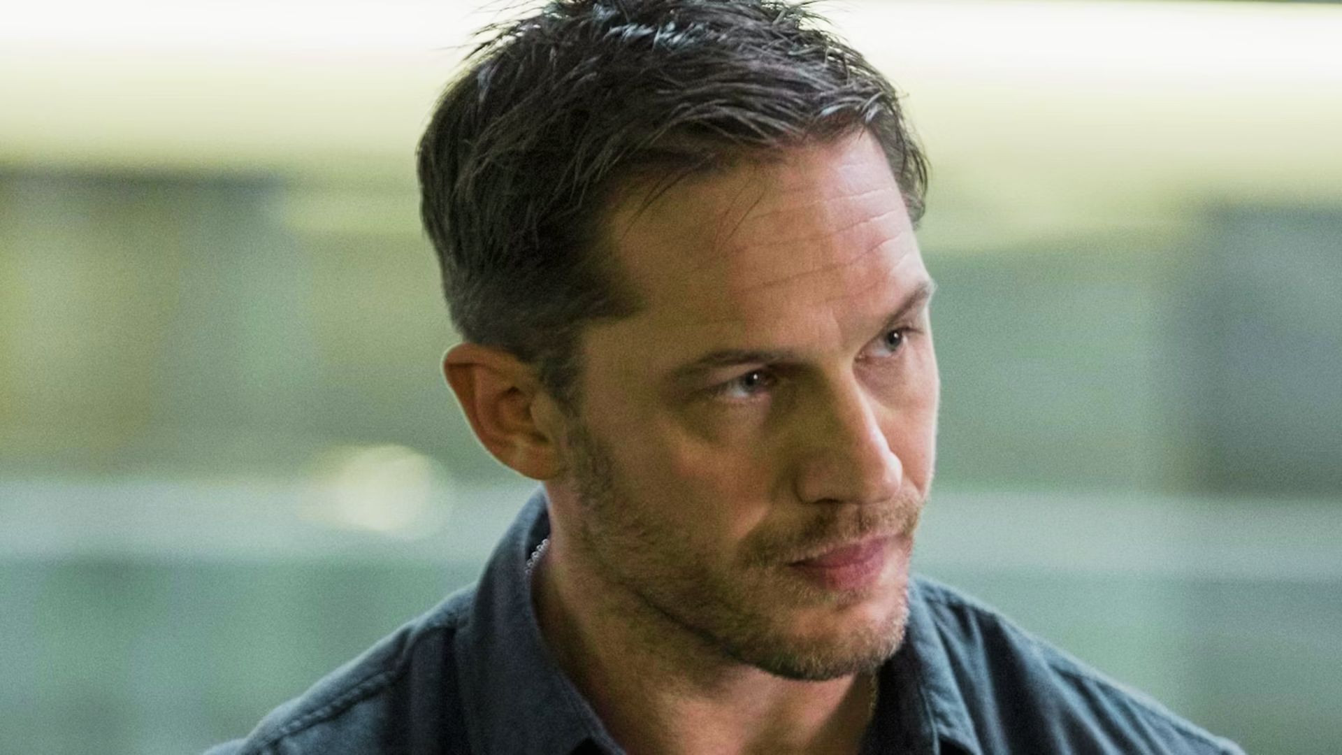 Tom Hardy with a neat side-part hairstyle and tapered sides in a blue shirt.