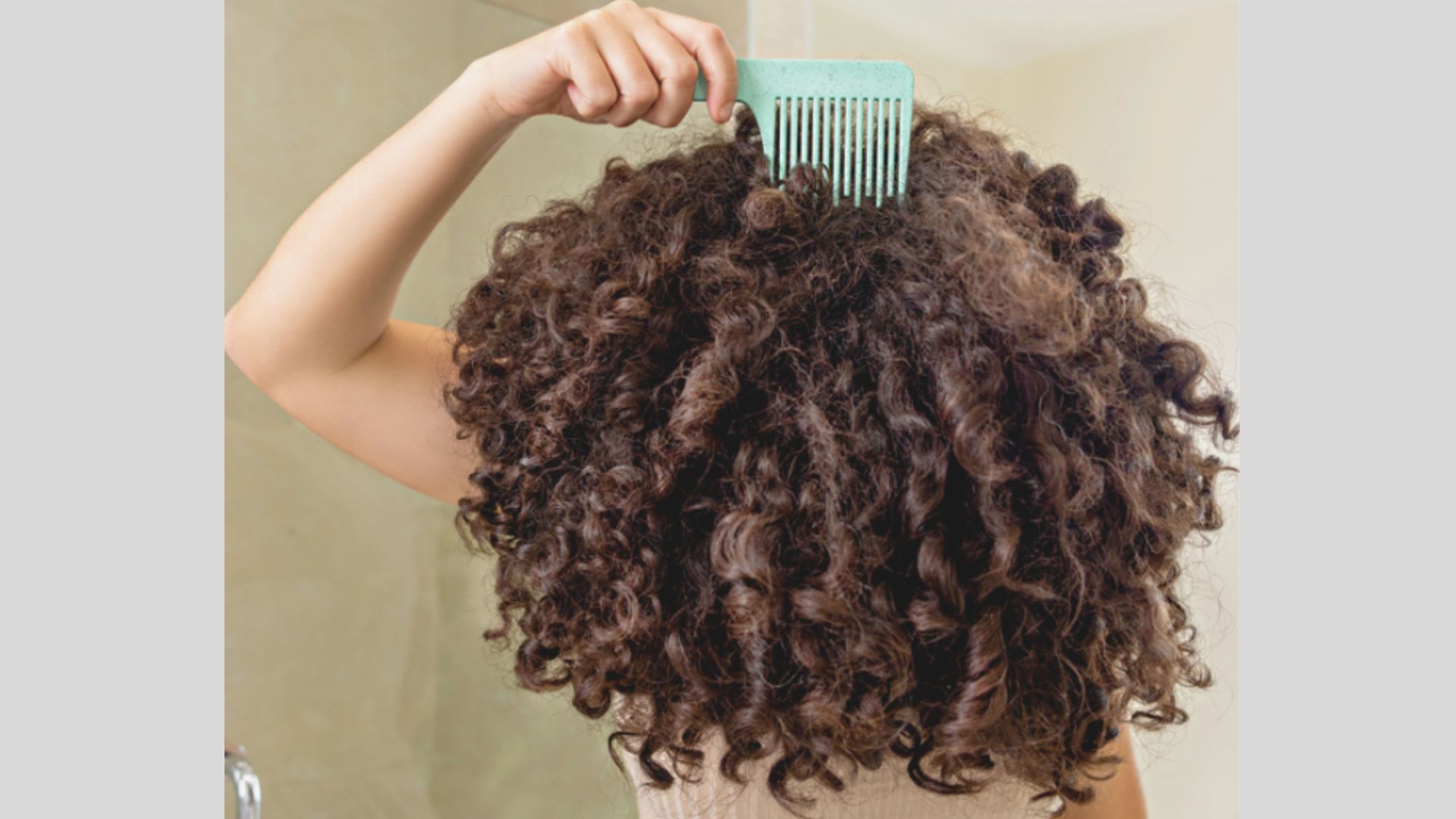 Back view of thick, dark brown curls being lifted with a wide-tooth comb for volume.