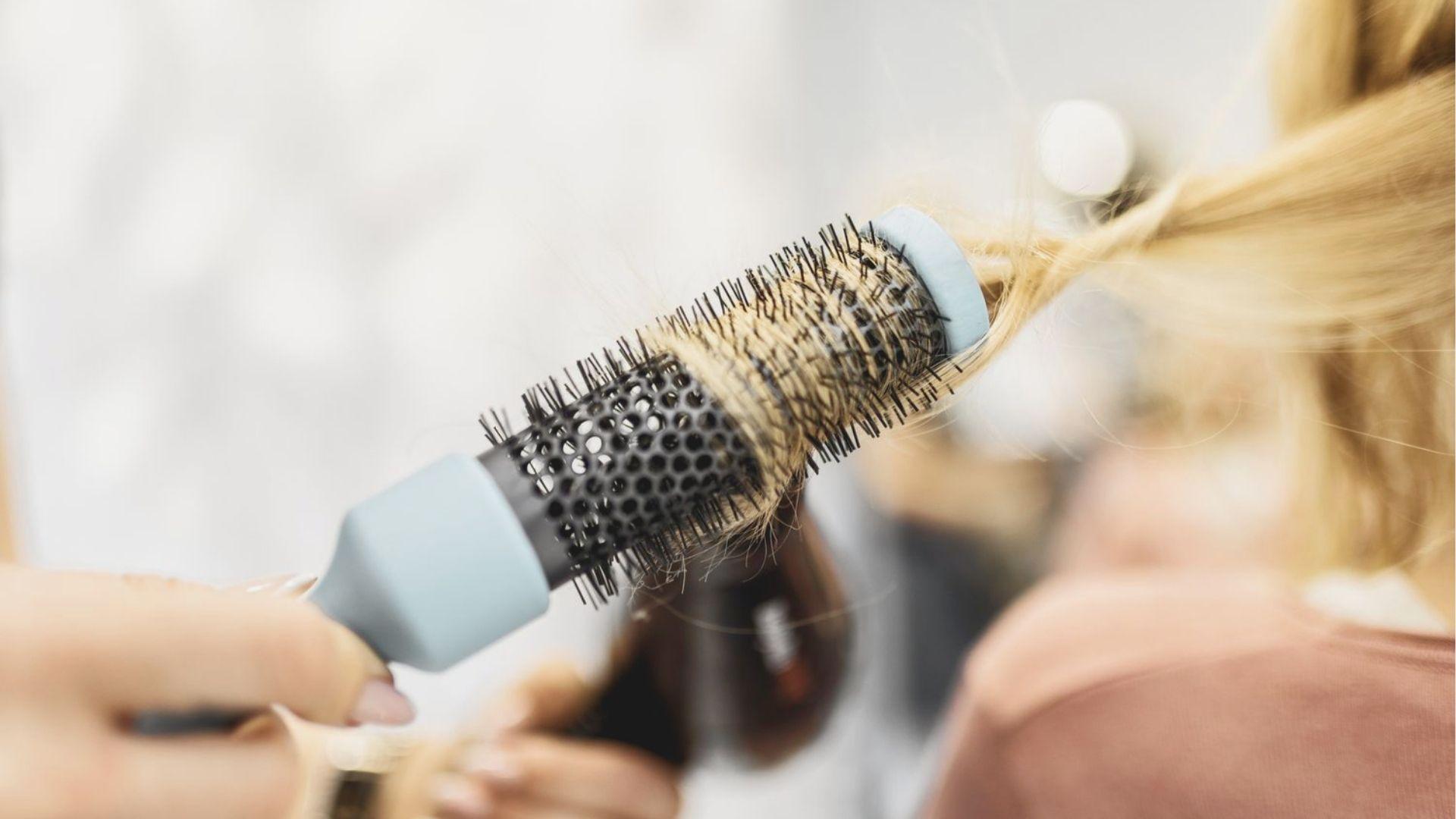 Close-up of a round brush curling blonde hair to create soft, voluminous waves.