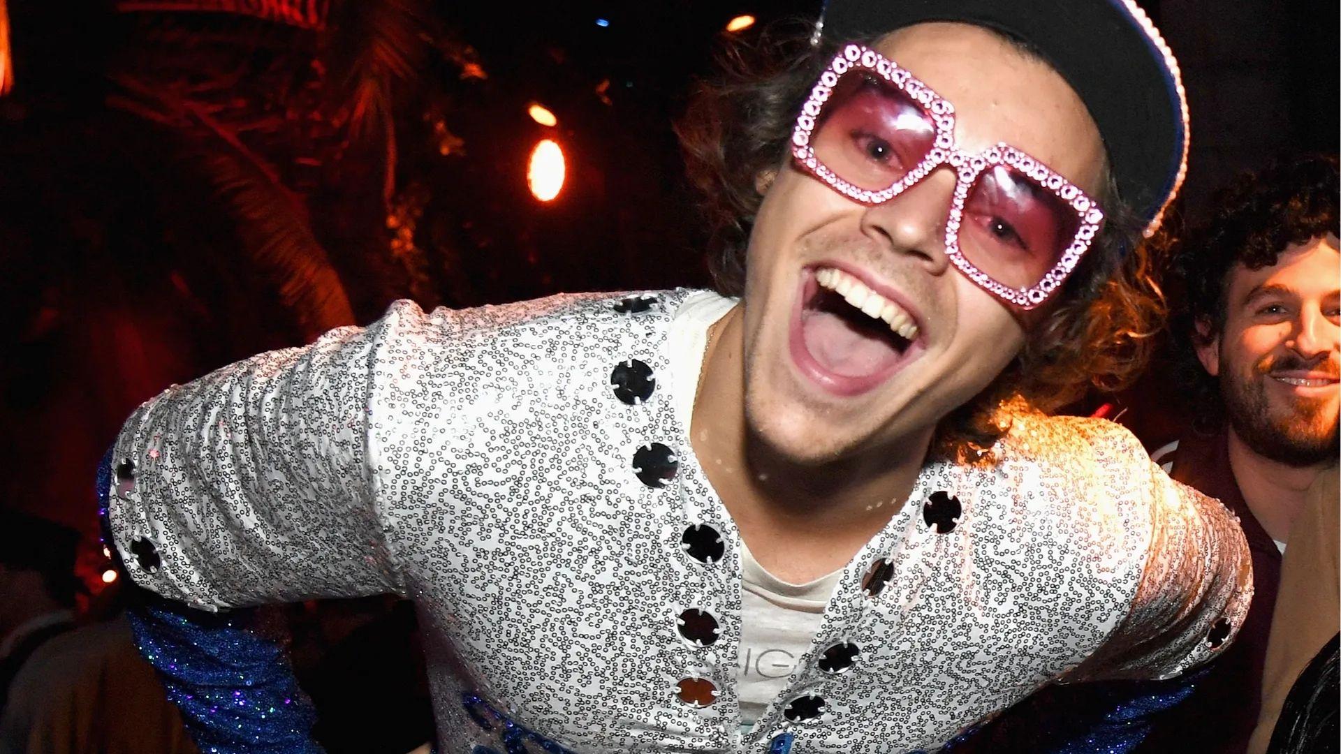 Harry Styles as Elton John in silver sequin jacket with oversized pink rhinestone glasses.