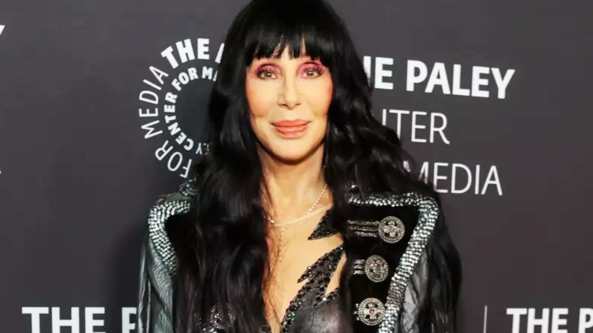 Cher at The Paley Center for Media smiling in a black leather jacket with silver studs and lightning bolt cutouts.