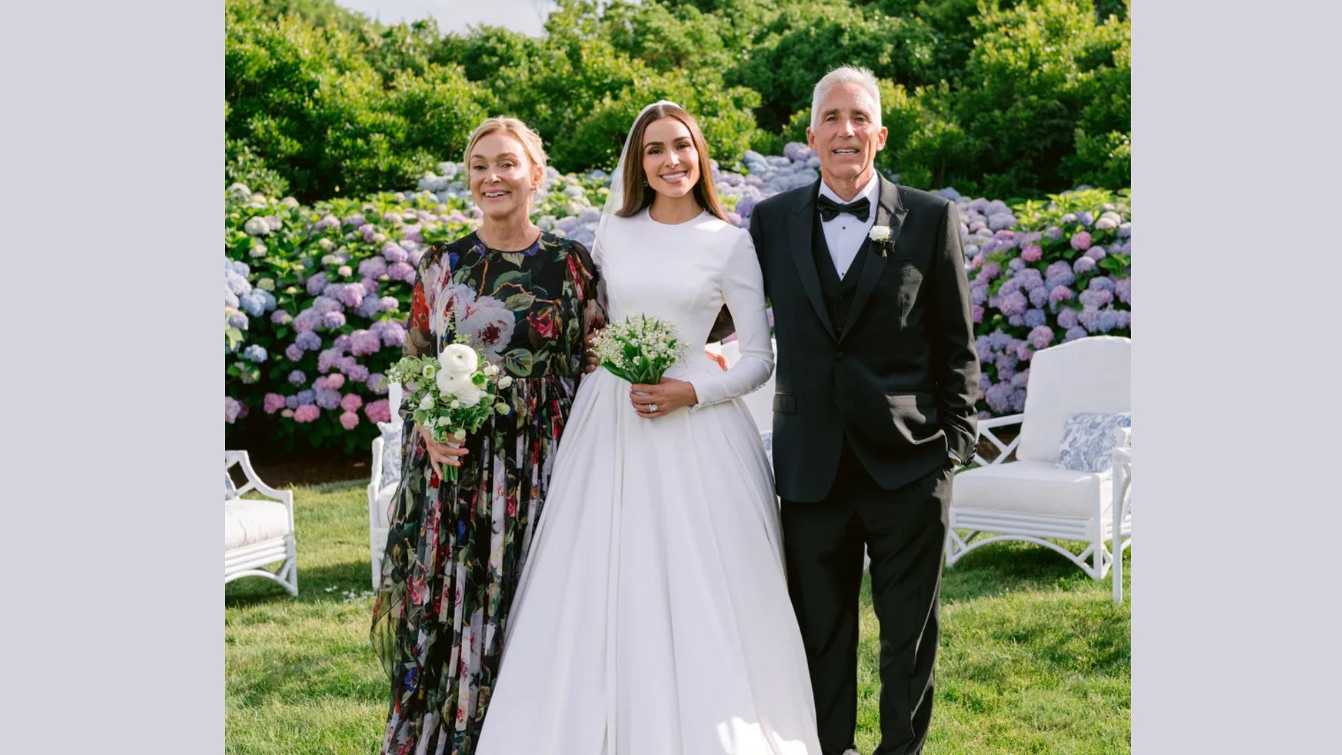 "A bride in a white dress stands between two smiling people in a garden, adorned with blooming hydrangeas. The mood is joyful and celebratory."