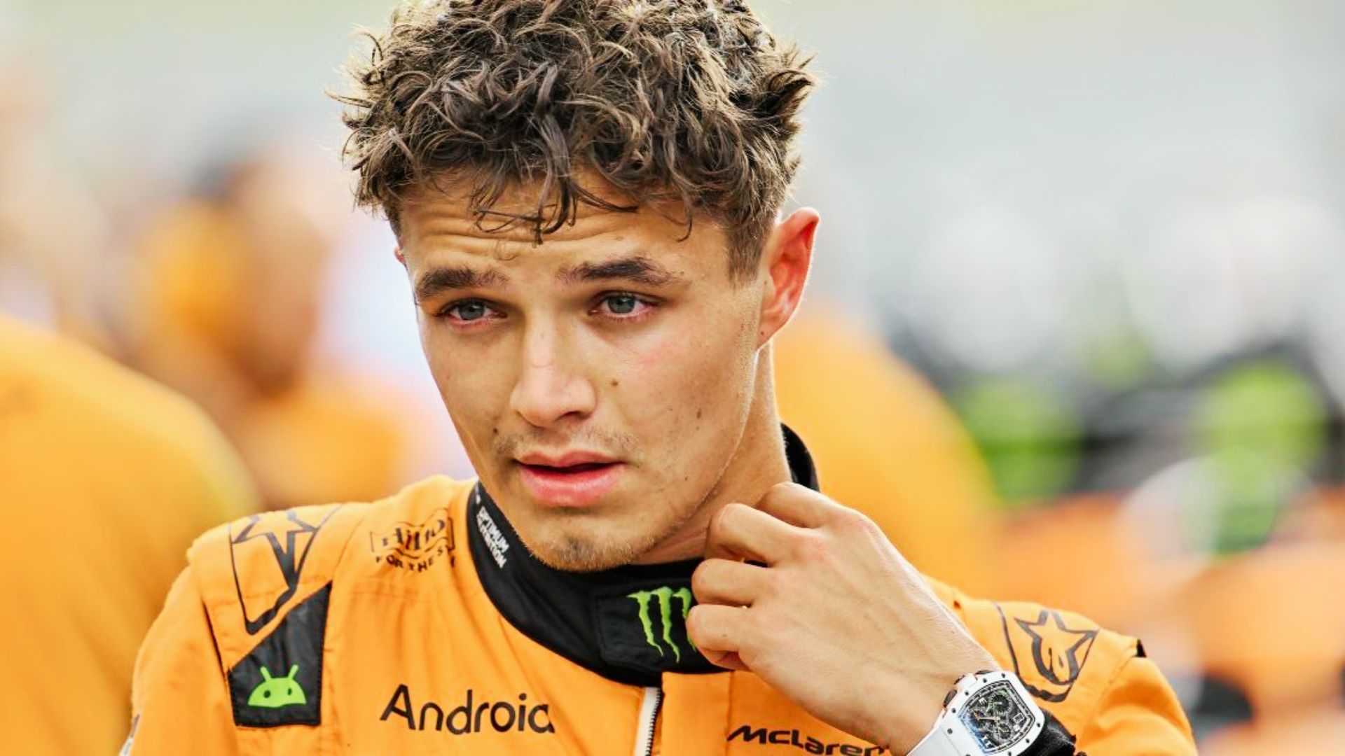 Lando Norris adjusts his race suit, sporting a textured curly top.