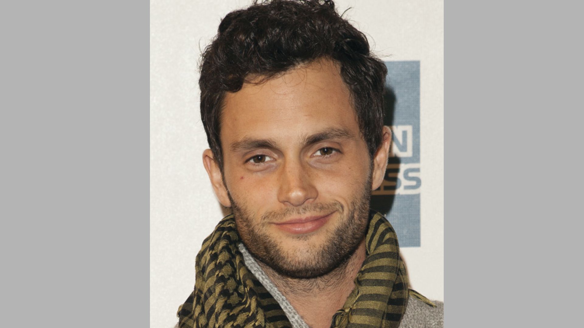 Penn Badgley wears a curly top with undercut sides and light stubble at red carpet event.