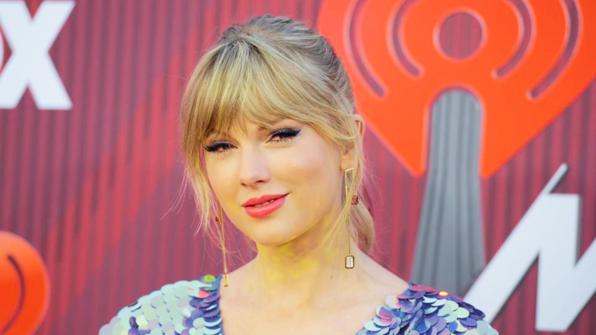 Taylor Swift on the iHeartRadio red carpet with honey blonde hair pulled into a loose updo with face-framing bangs.
