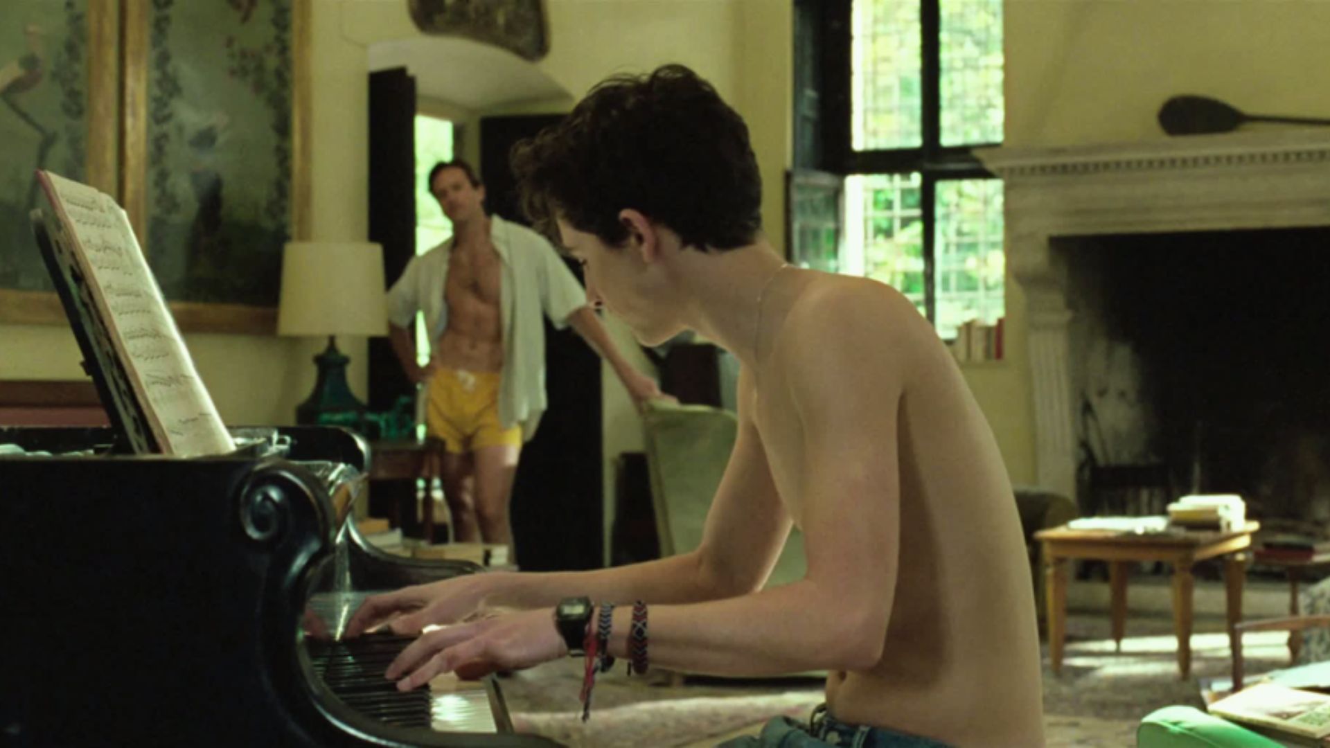 "A shirtless man playing the piano in a cozy living room, surrounded by warm lighting and comfortable furniture."
