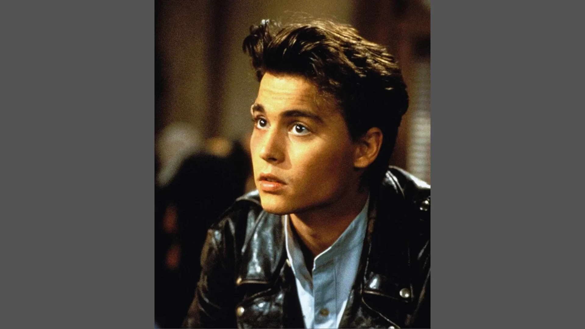 Young Johnny Depp with 90s natural tousled waves 21 Jump Street Look hairstyle wearing black leather jacket over light blue collared shirt.