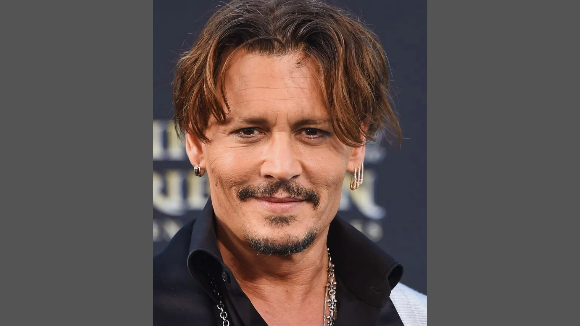 Johnny Depp with layered tousled brown hair, goatee, and multiple earrings wearing black shirt and silver necklaces.