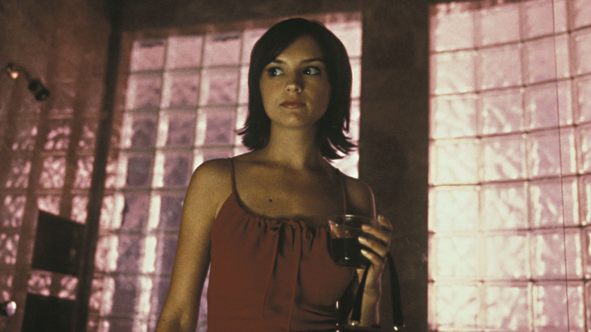 A woman in a red dress elegantly holds a glass, showcasing a poised and sophisticated demeanor."
