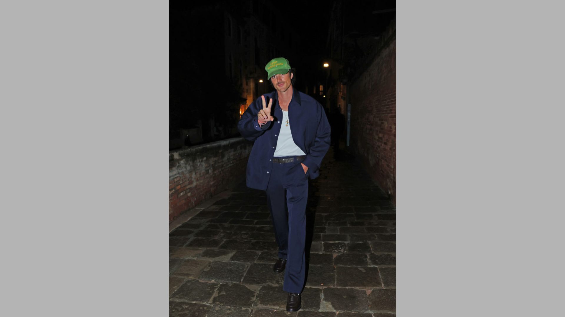 A man in a suit and green hat walks confidently down a city street, surrounded by urban scenery.