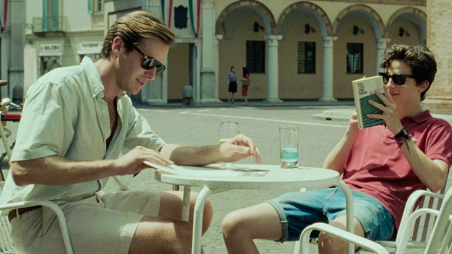Two men seated at a table, engaged in conversation with a book and a drink in front of them."