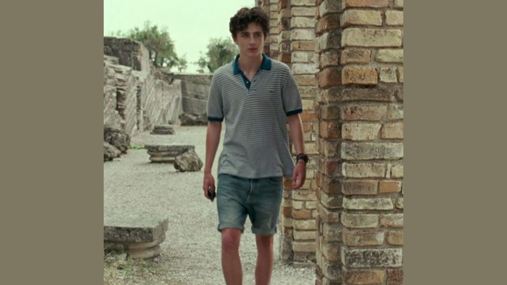 A young man wearing blue shorts and a polo shirt stands casually, smiling at the camera."