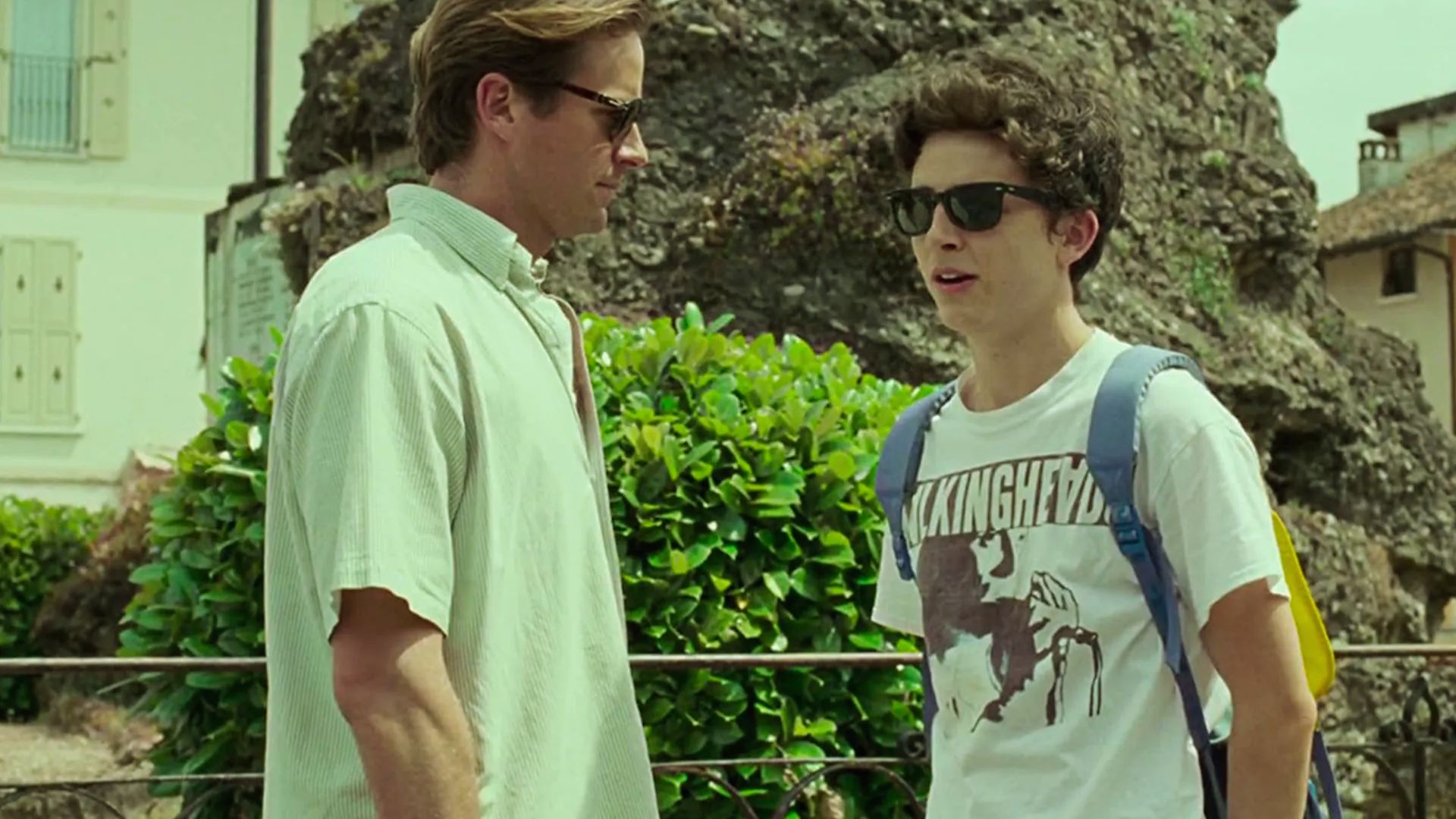 Two men wearing sunglasses engaged in conversation outdoors."