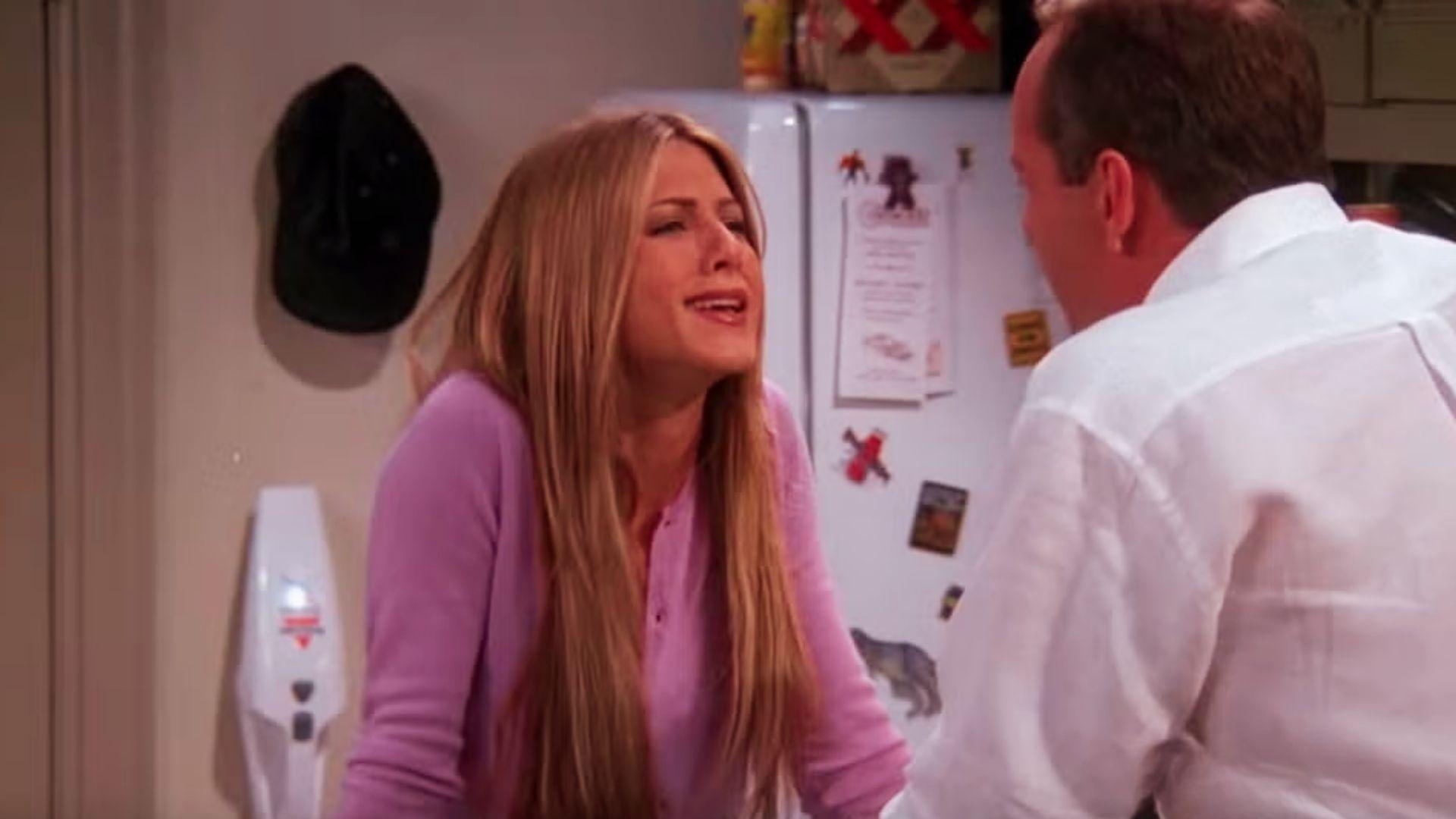 Rachel Green with ultra-long sleek straight blonde hair, wearing purple cardigan, talks intensely in Monica’s kitchen.