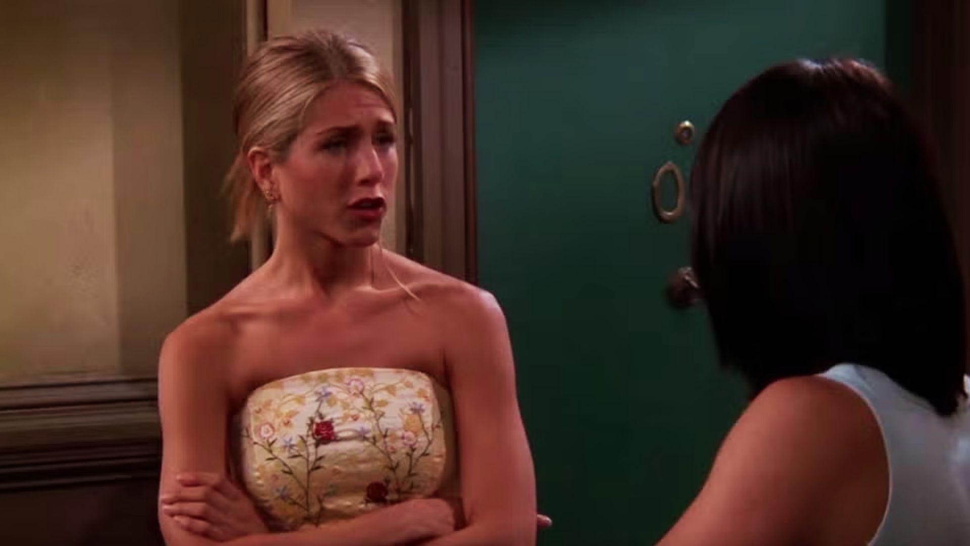 Rachel Green with sleek blonde ponytail in strapless floral dress talks to Monica by apartment door.