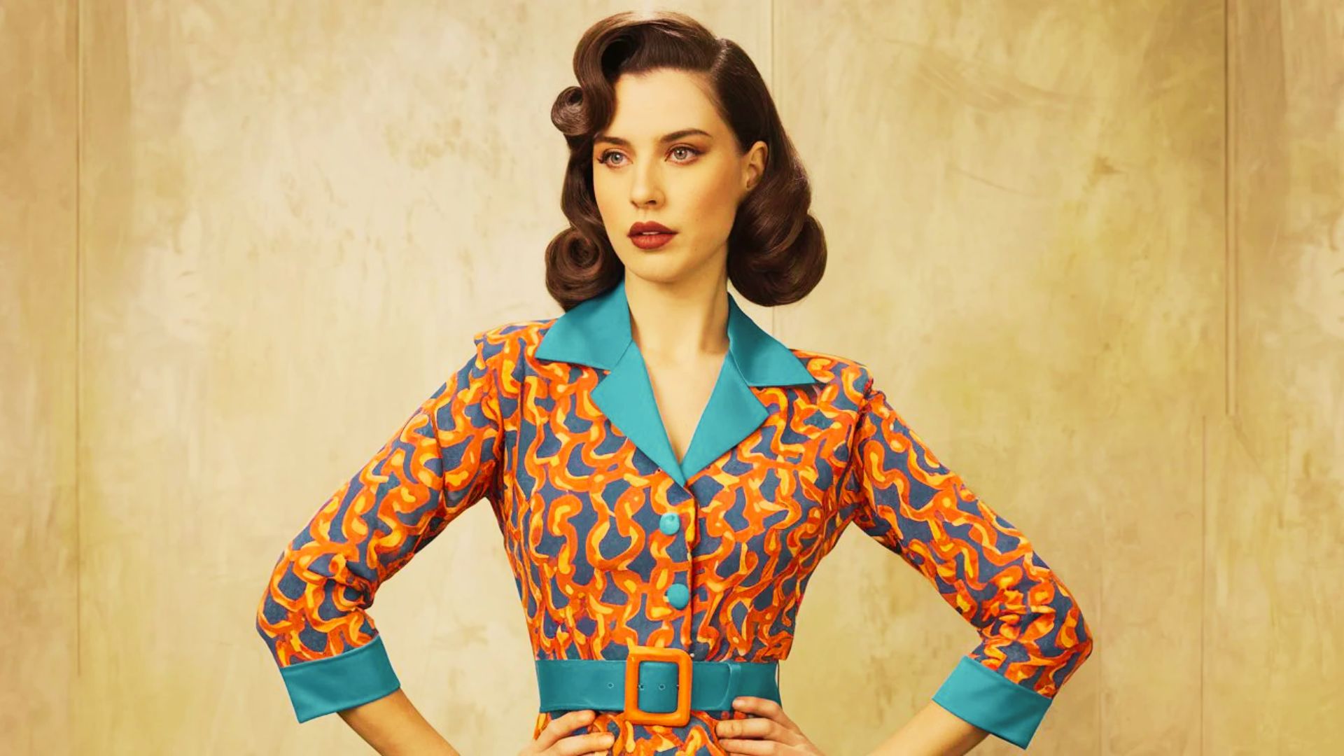 Woman with victory rolls wears a bold orange and blue 1960s print dress with a teal collar and belt.