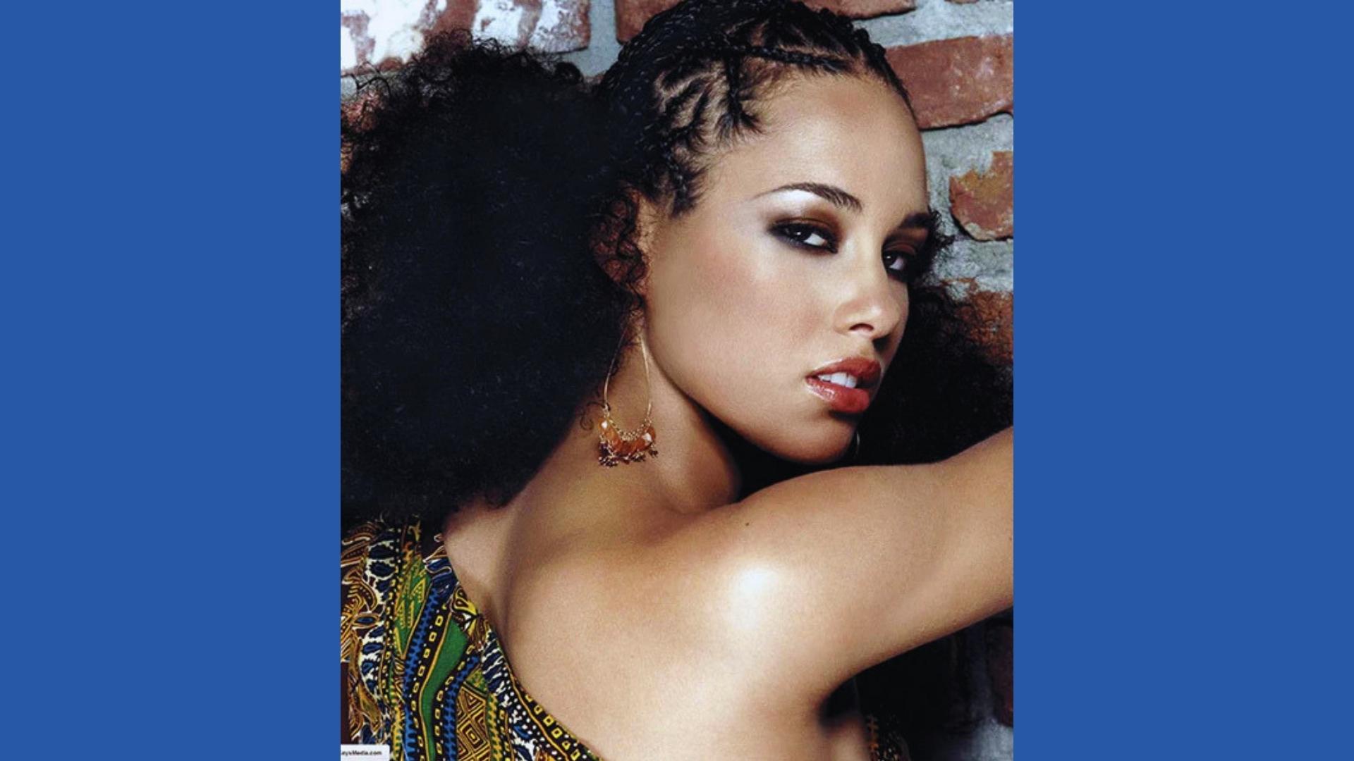 Young Alicia Keys poses in patterned dress with braided cornrow crown and big natural afro puff, ornate earrings, smoky eyes.