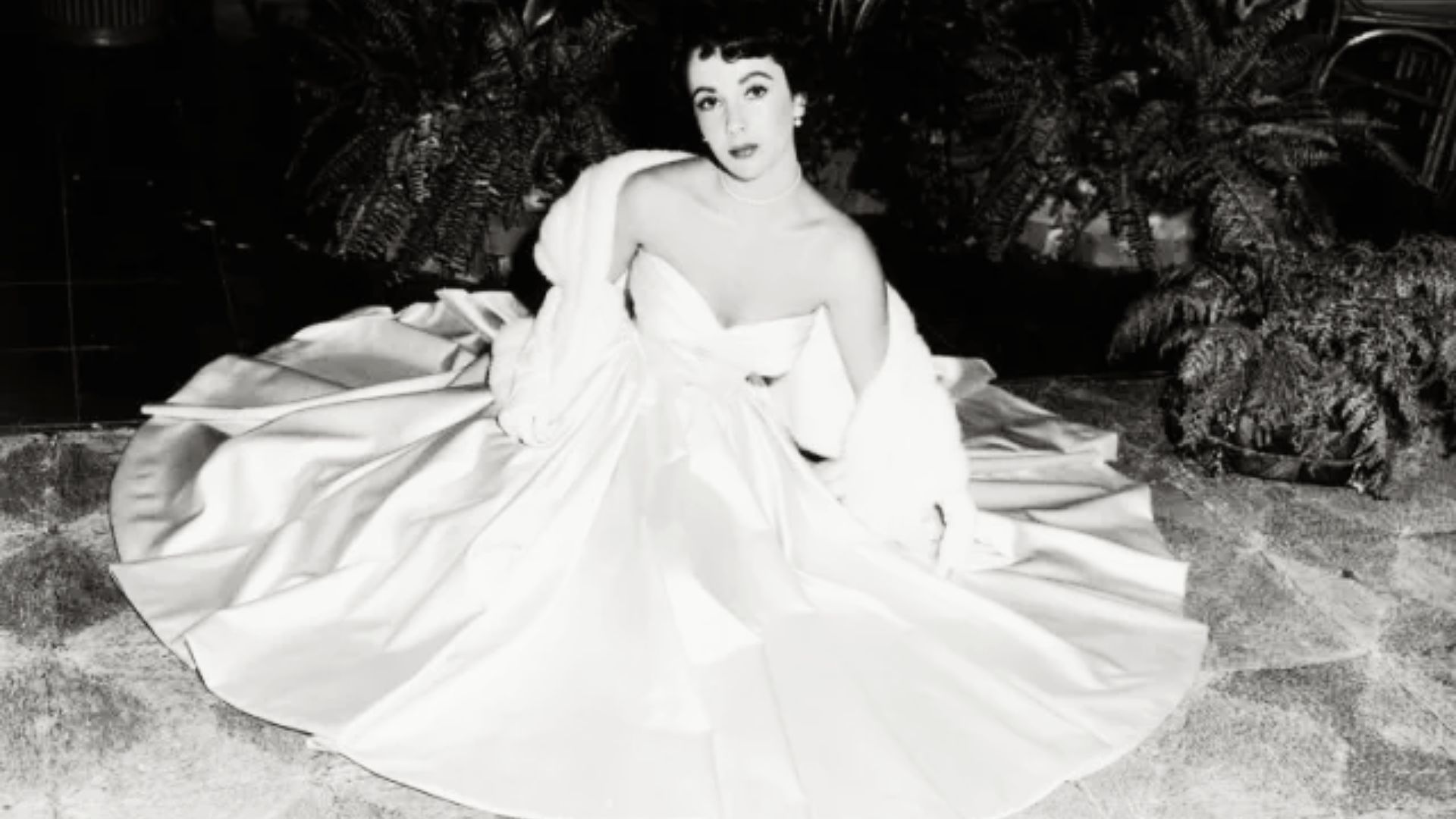 Black and white portrait of Elizabeth Taylor in a strapless satin ball gown with a fur stole.