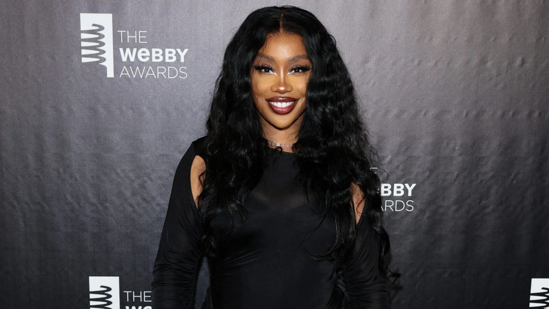 Long black loose waves influenced by SZA hairstyles, featuring a center part and soft, glamorous texture at a red carpet event.