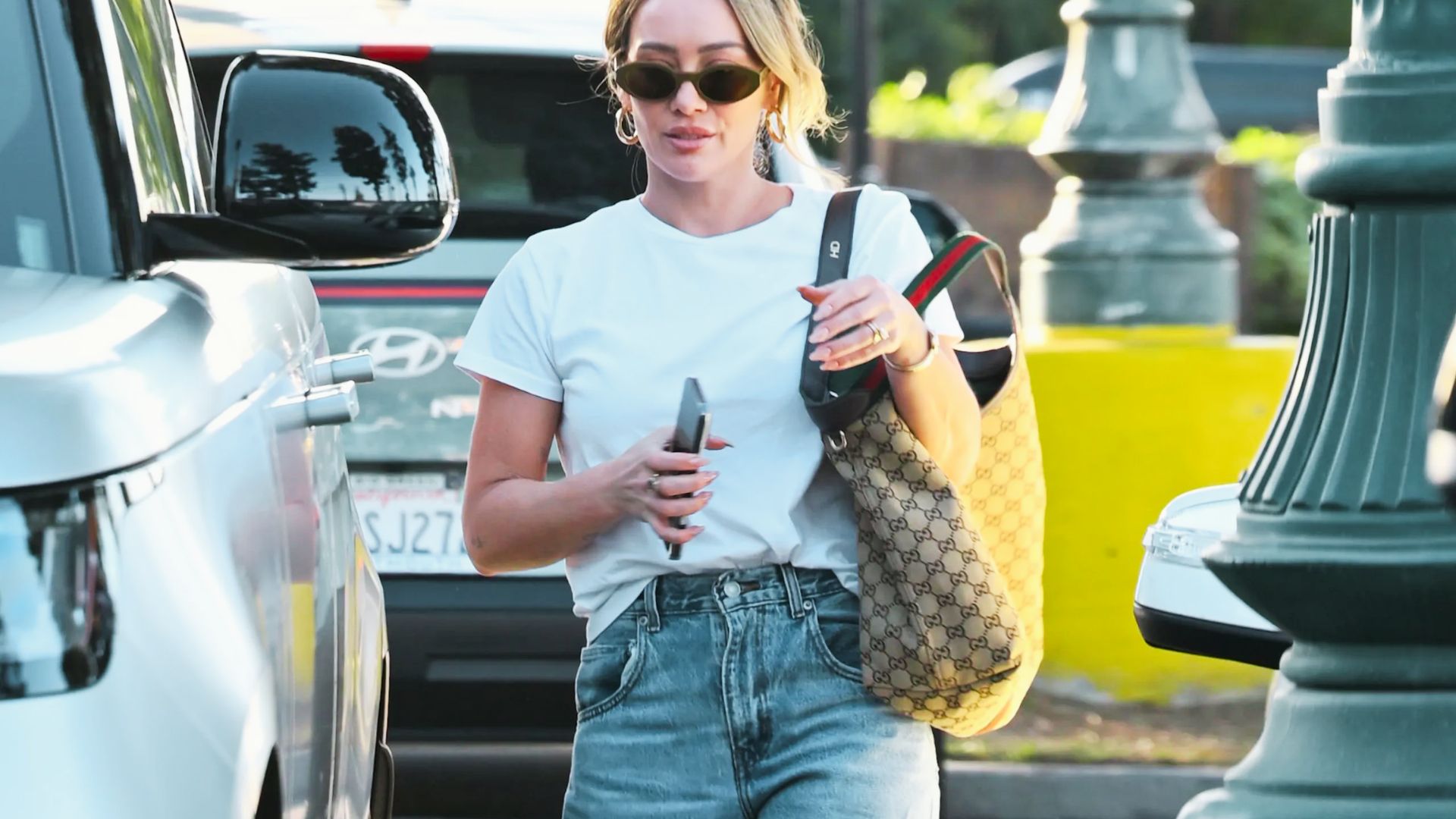 Hilary Duff walks curbside in a casual white tee tucked into high-waisted jeans.