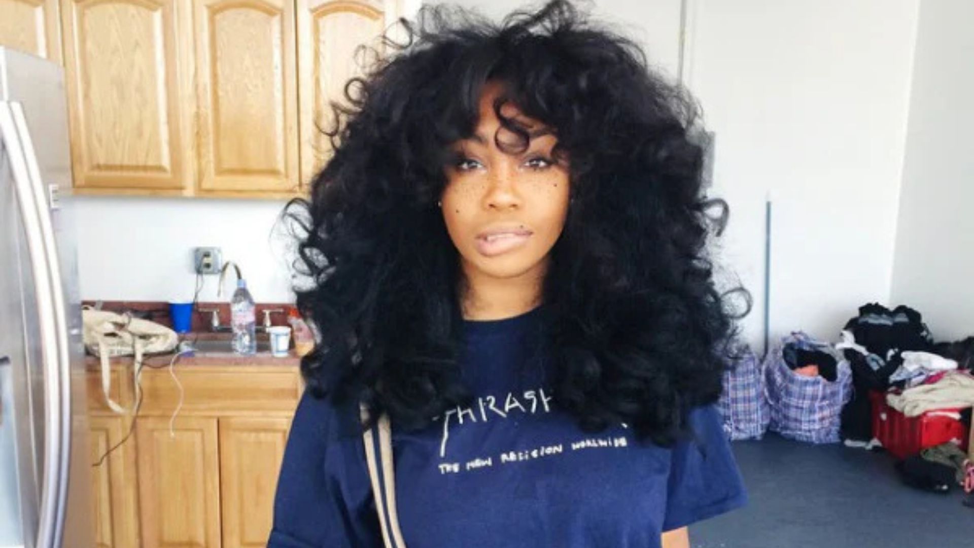 Voluminous natural curly hairstyle with soft bangs, influenced by SZA's signature big curls and textured hair looks.