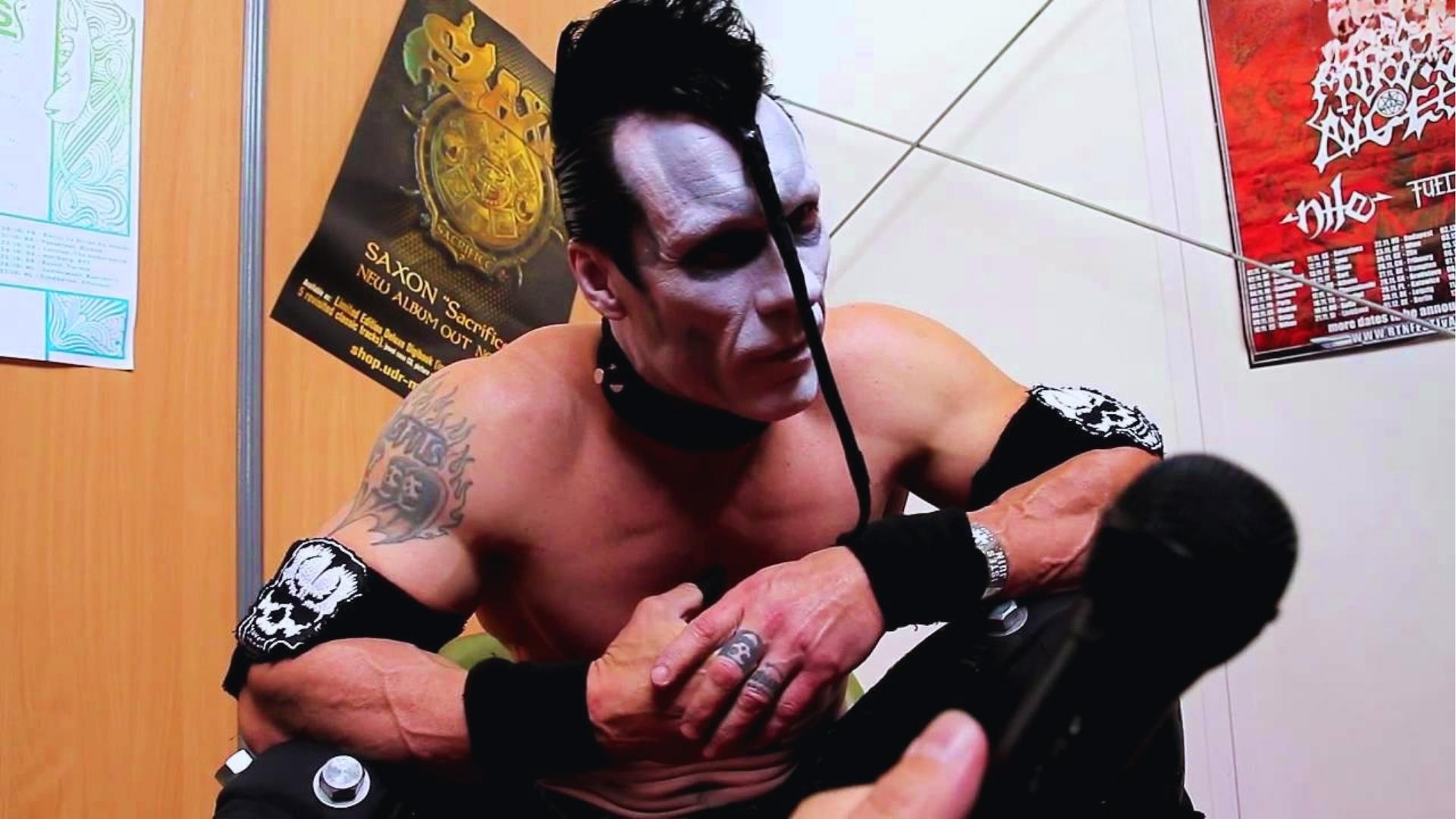 Doyle Wolfgang von Frankenstein sits backstage in full white face paint, devilock, and skull armbands, leaning forward during the interview.