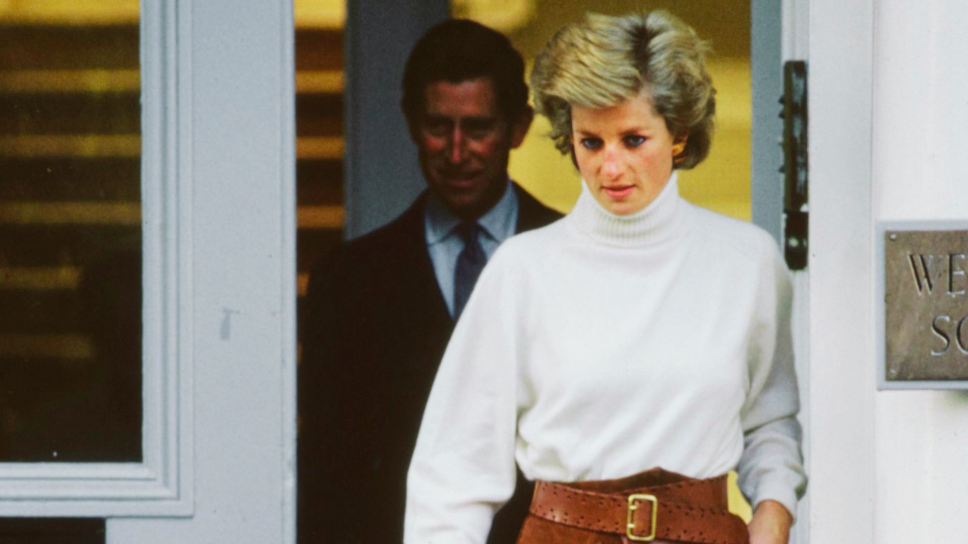 Princess Diana exits a building in a crisp white turtleneck sweater tucked into high-waisted pants.