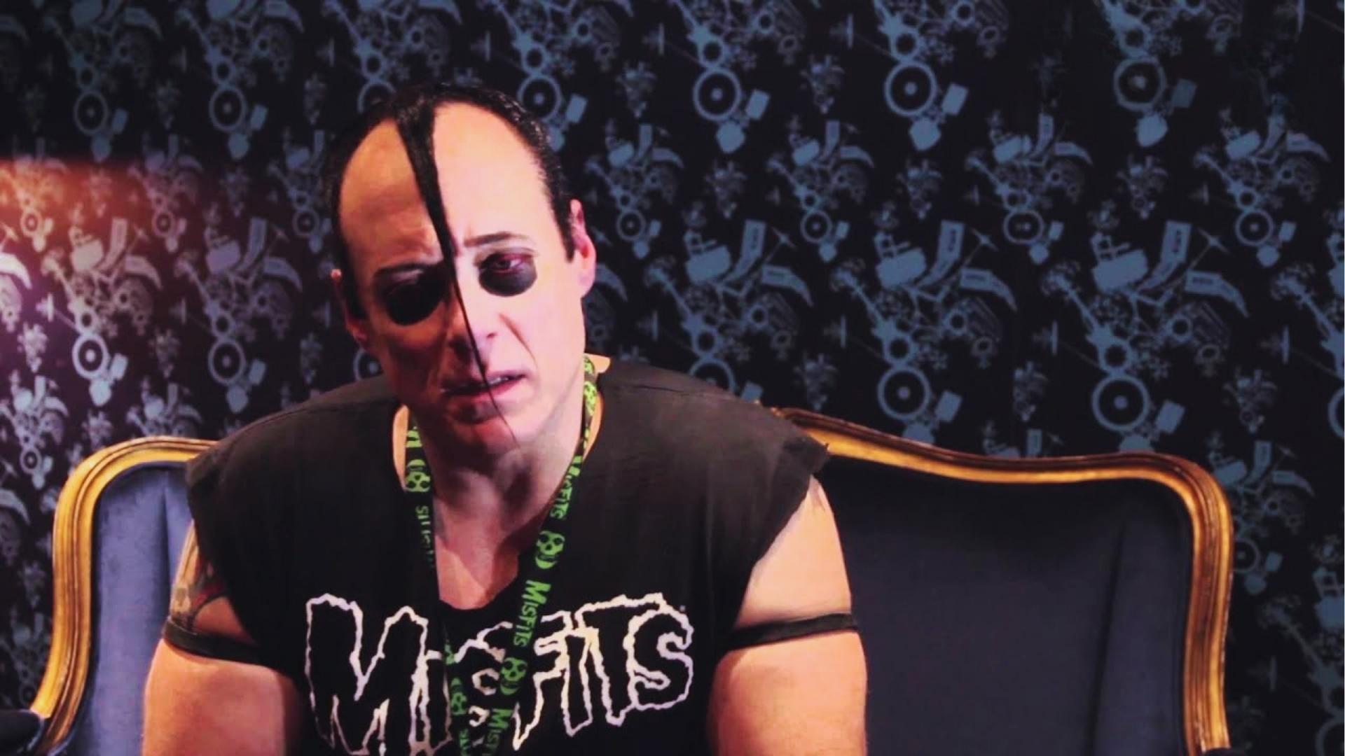 Doyle Wolfgang von Frankenstein wears Misfits tee with half black eye makeup and devilock hairline during interview on couch.