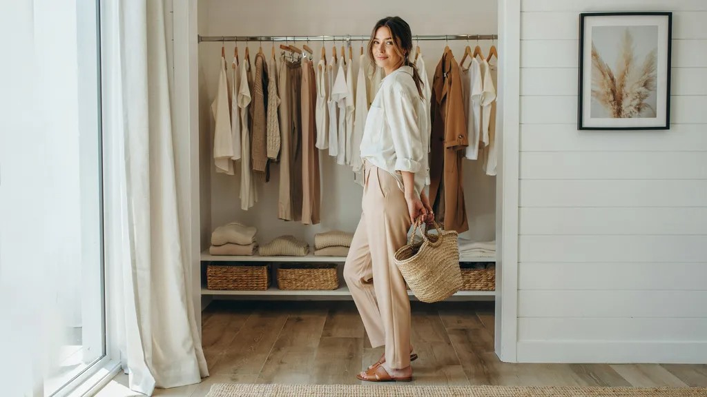 Woman admiring a neatly organized coastal capsule wardrobe at home.