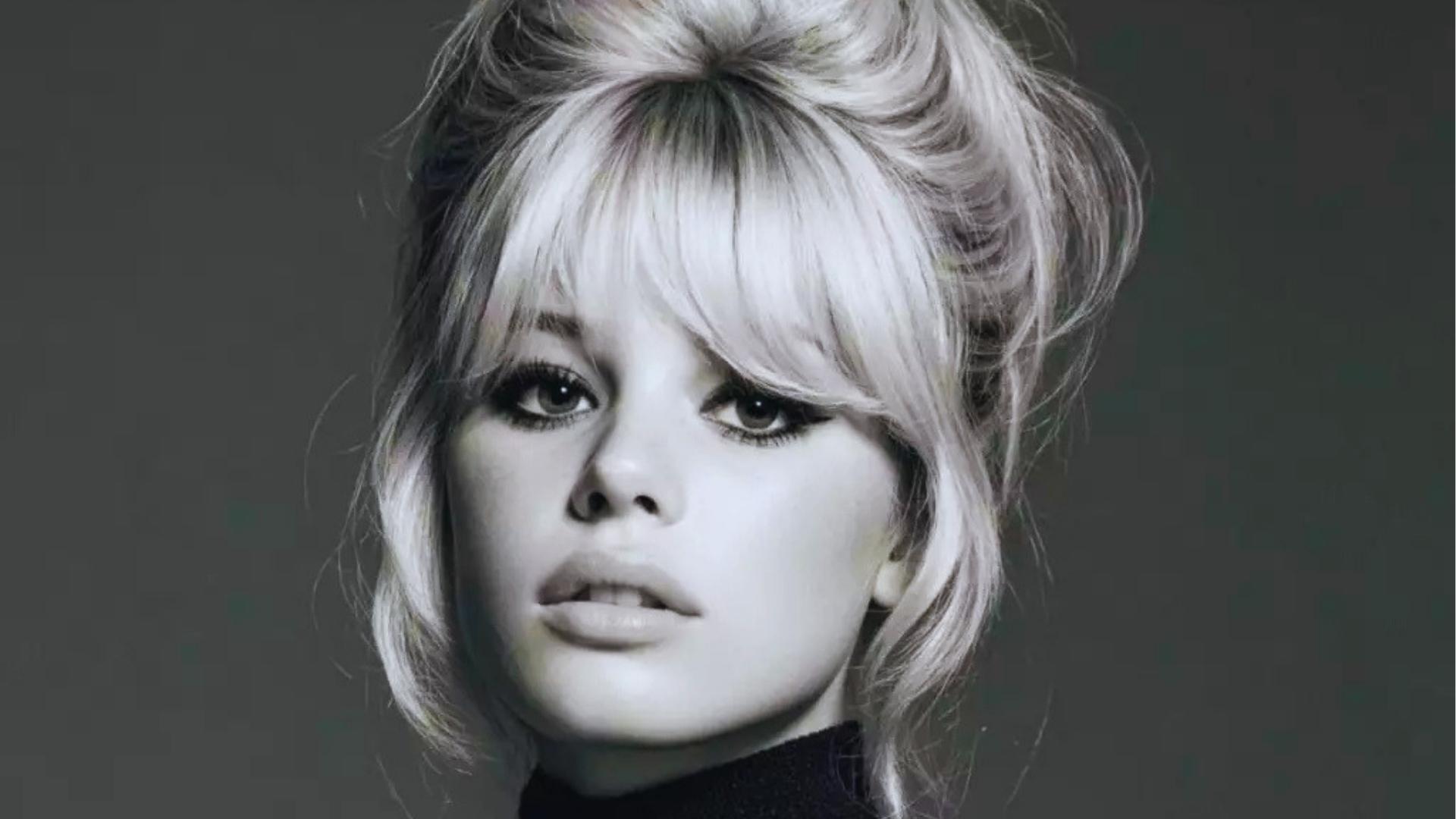 Black and white portrait of Brigitte Bardot with iconic 1960s tousled updo, heavy curtain bangs, and sultry cat-eye makeup.