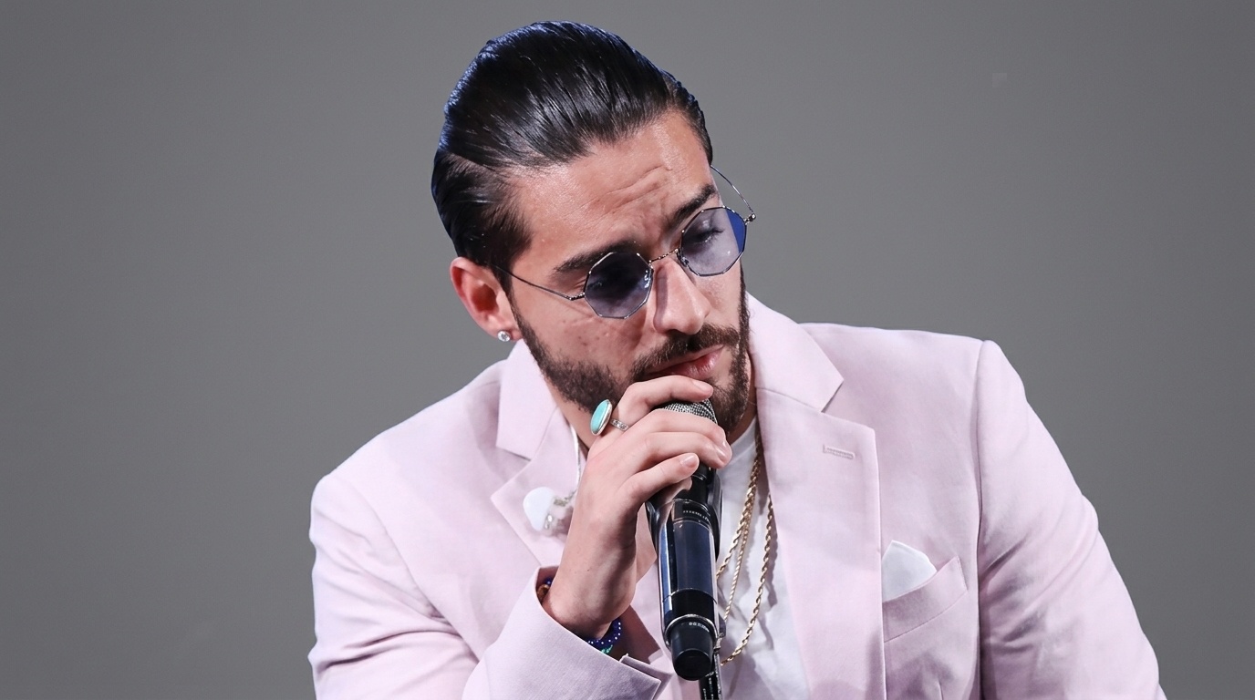 Maluma with slicked Back man bun hair in low ponytail wearing pink suit and glasses