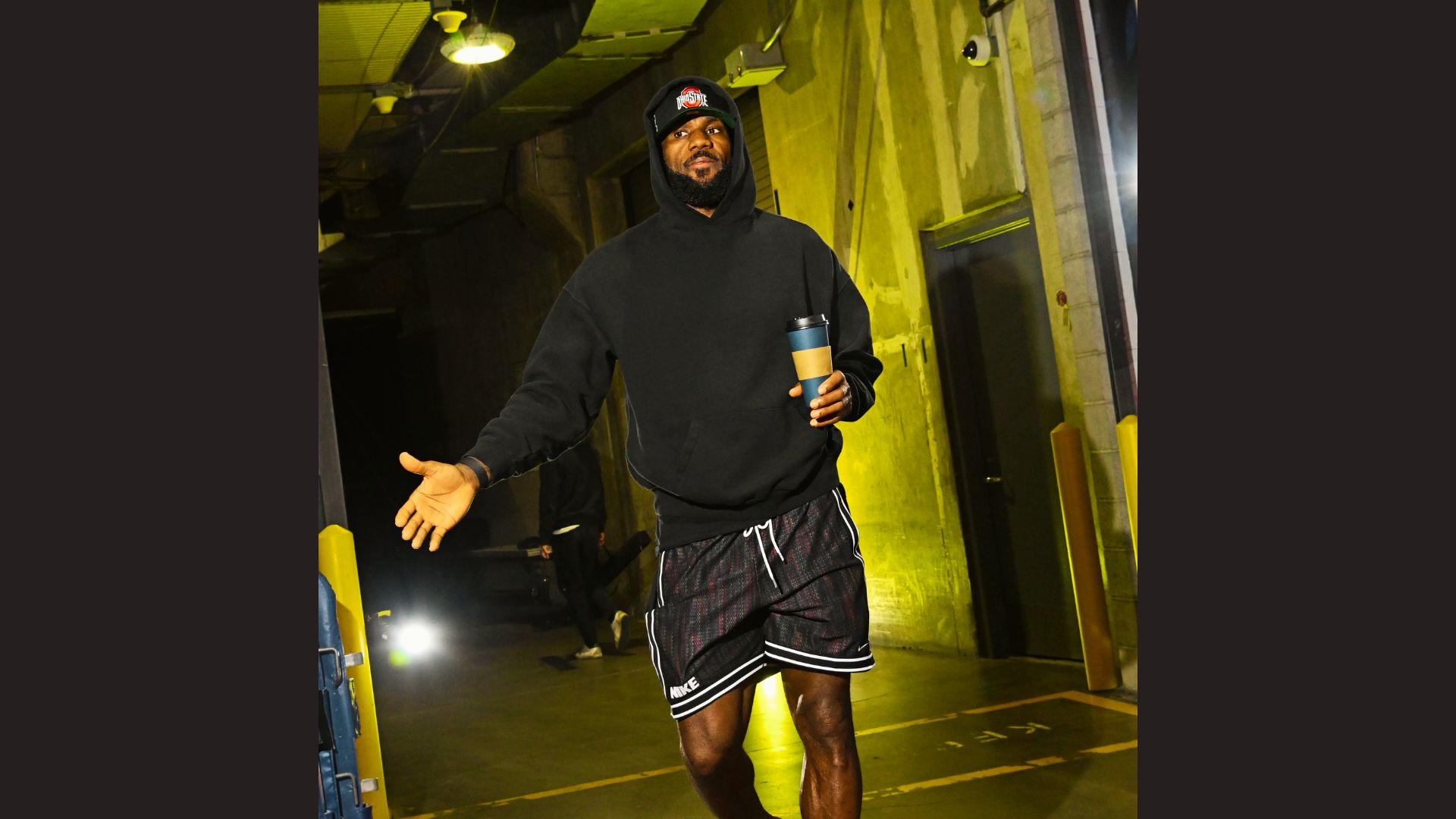 LeBron James wearing a tailored blazer and sneakers in an arena tunnel.