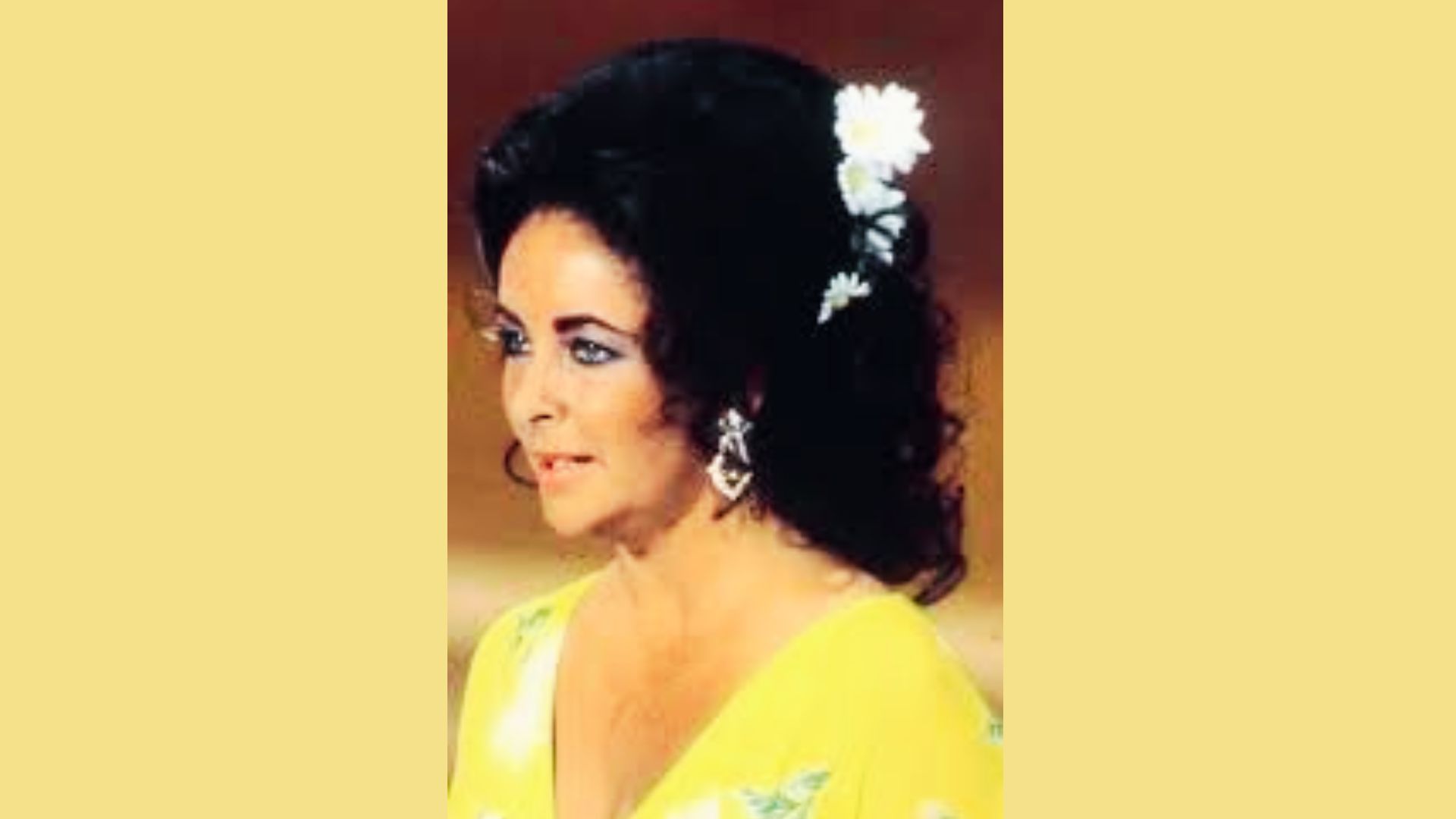 Close-up of Elizabeth Taylor in a yellow floral dress with daisies in her hair and statement earrings.
