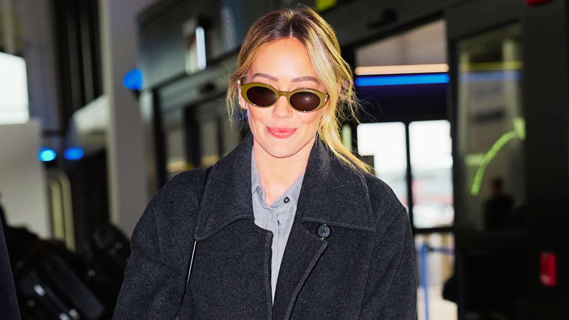 Hilary Duff wears an oversized charcoal wool coat over a gray button-up for airport style.