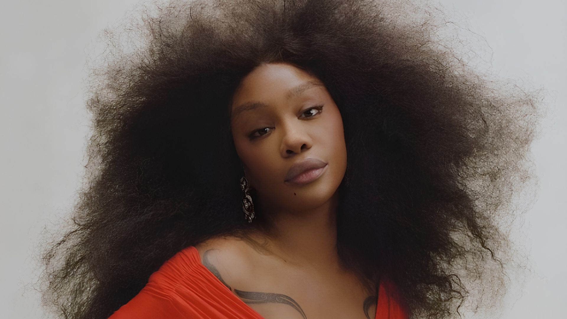 Sza with large, natural curls wearing a vibrant red top, showcasing her confident and stylish look.
