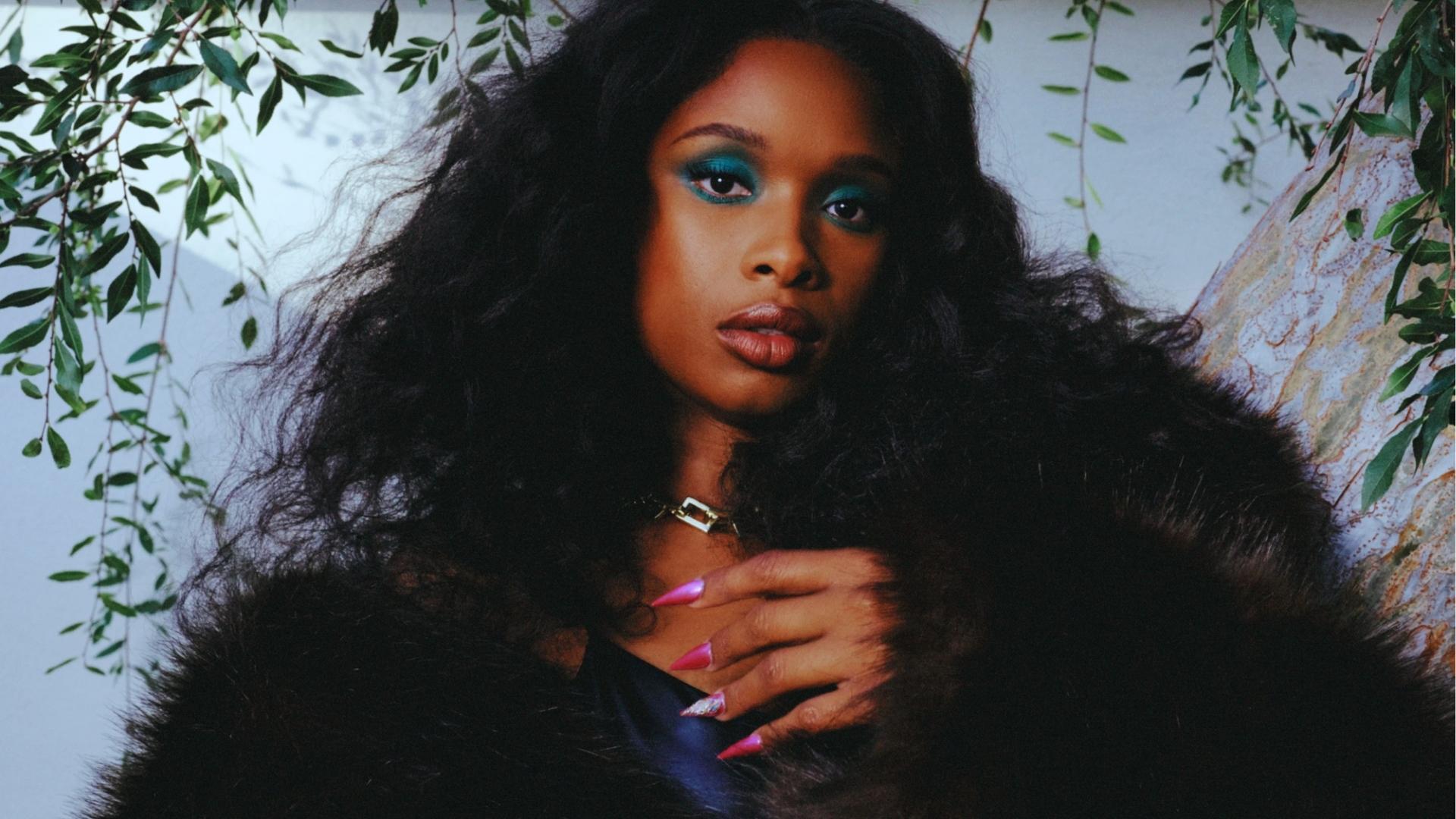 Jennifer Hudson in black fur coat with teal eyeshadow and hot pink nails, posing under a tree with full natural curls.