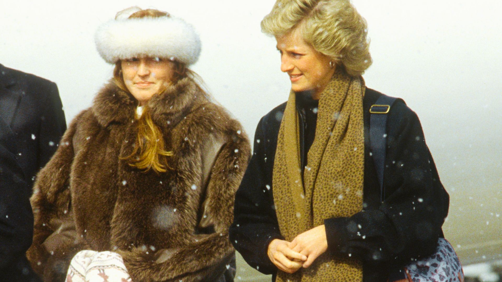 Princess Diana walks in the snow wearing a black coat and patterned tan scarf.