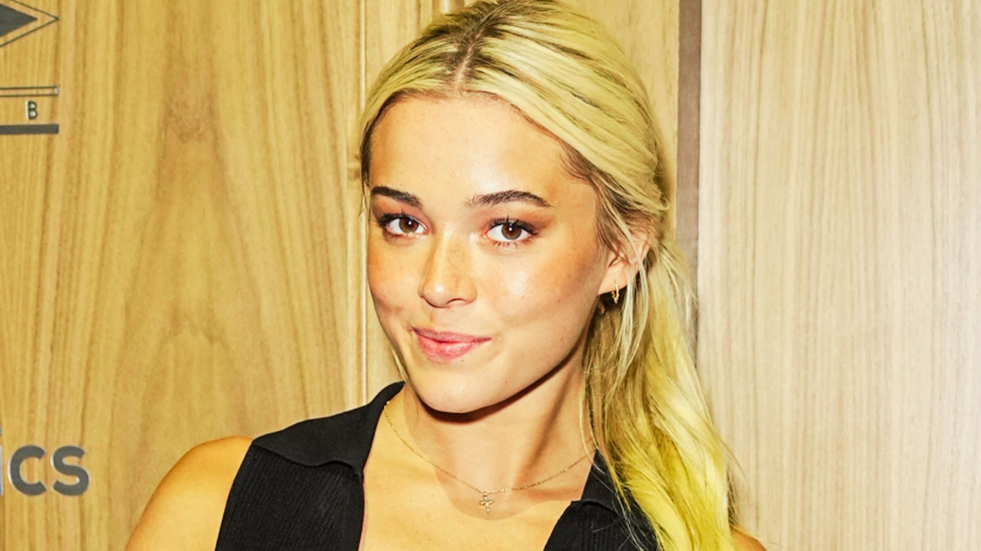 Livvy Dunne poses in a black top against a wooden backdrop at an event.