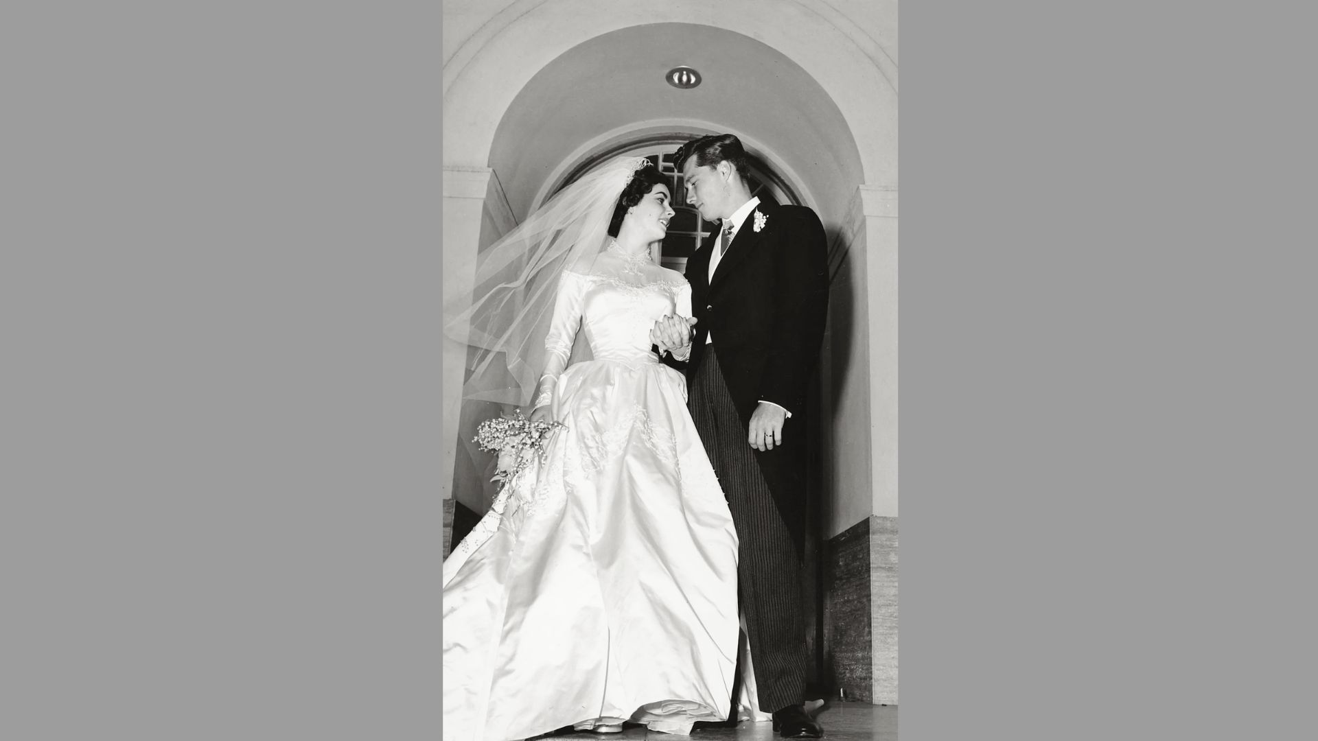 Elizabeth Taylor in her 1950 wedding gown designed by Helen Rose, holding a bouquet beside groom Conrad Hilton Jr.
