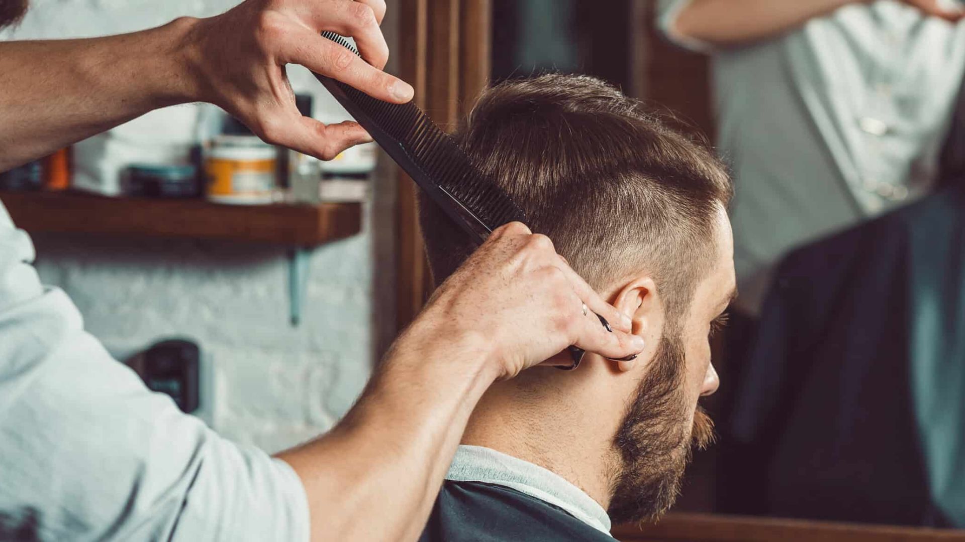 Barber combing and cutting a man's dark brown hair with a taper fade in a barbershop.