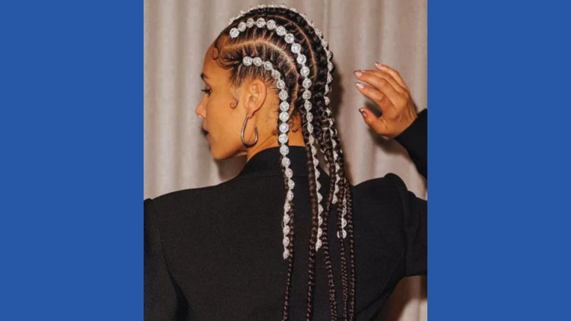 Rear view of Alicia Keys showcasing long box braids adorned with crystal embellishments along each braid, black blazer, silver hoops.
