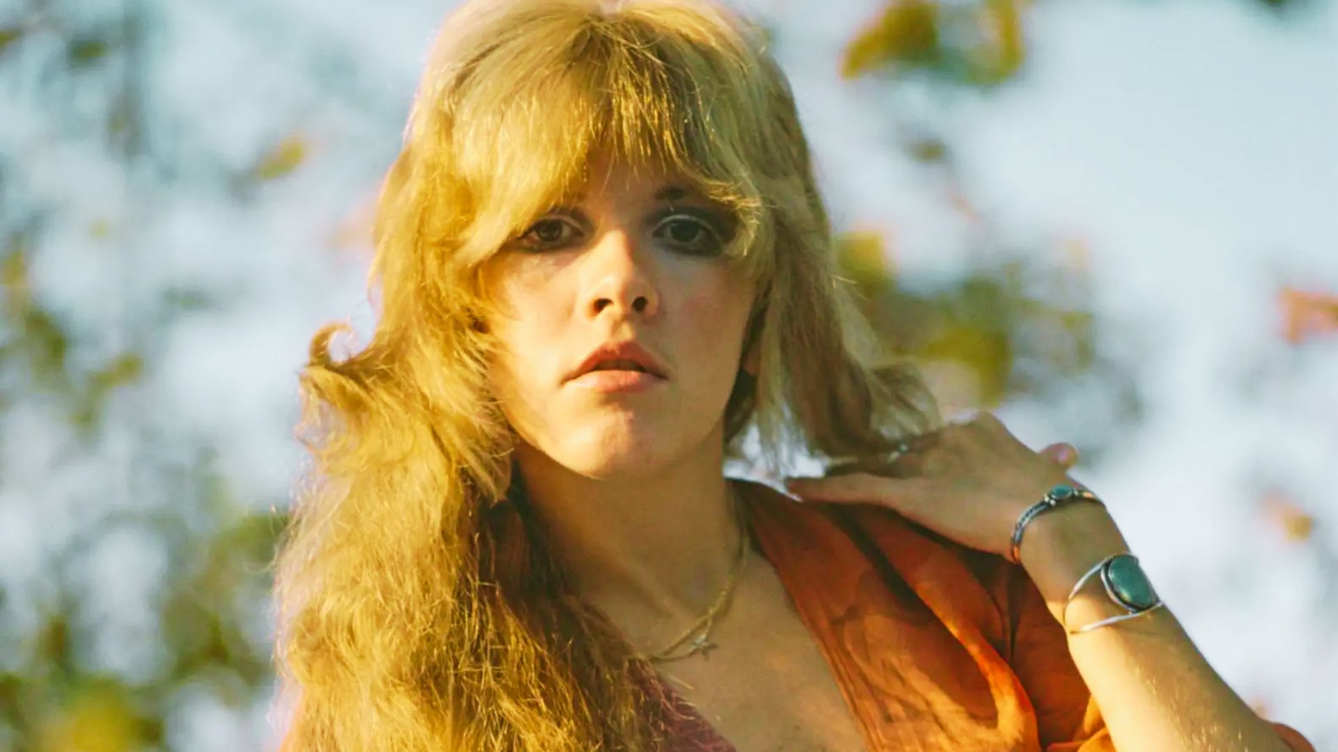 Outdoor portrait of Stevie Nicks with sunlit, golden blonde hair in a soft, layered shag cut with long curtain bangs.