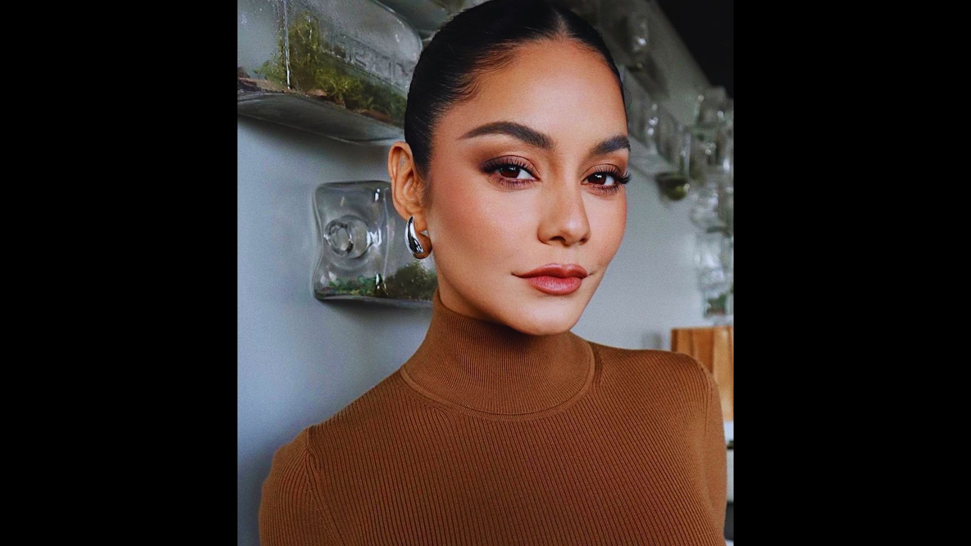 Woman with almond eyes and winged eyeliner wearing a brown turtleneck sweater.