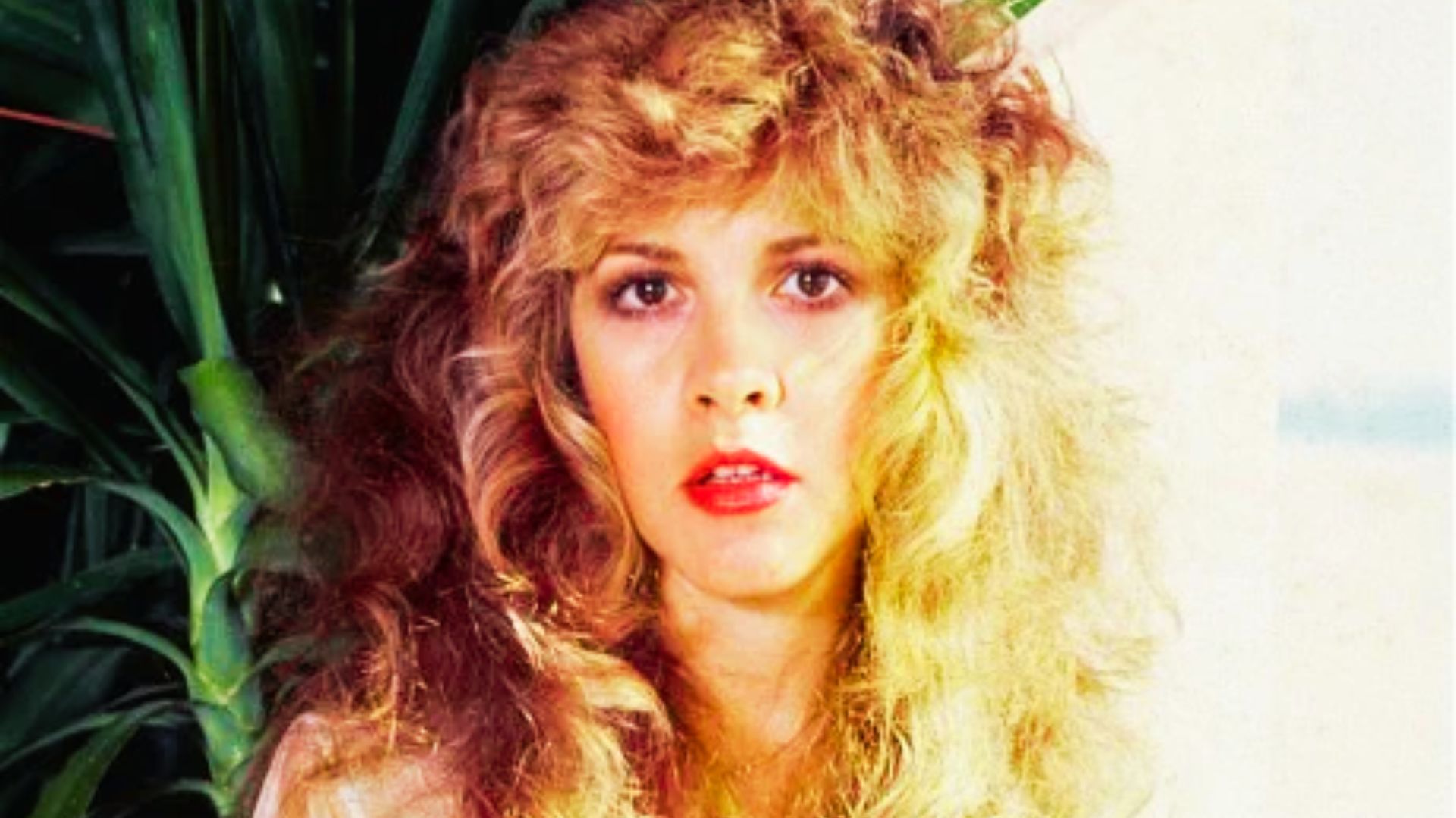 Color portrait of Stevie Nicks with big, blown-out blonde curls and heavy feathered bangs framing her face.