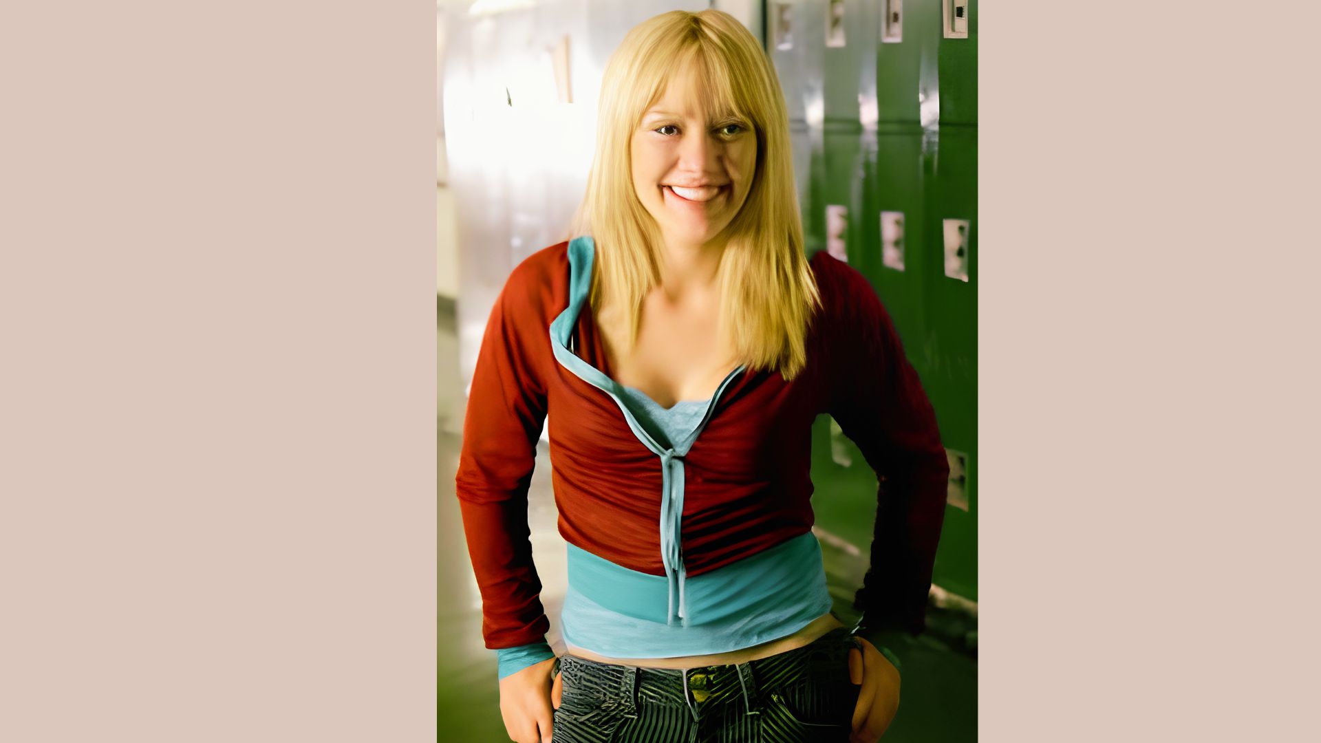 Teen Hilary Duff smiles by school lockers in a red zip-up hoodie over a blue tank top