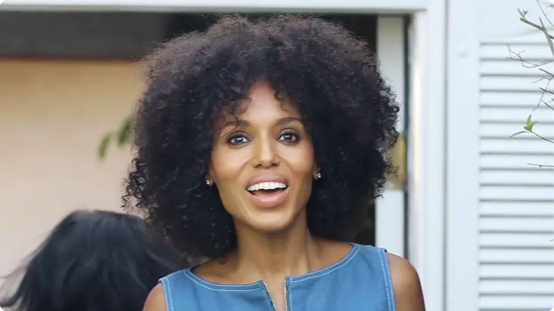 Kerry Washington smiling in sleeveless denim top showing natural curly afro hair outdoors