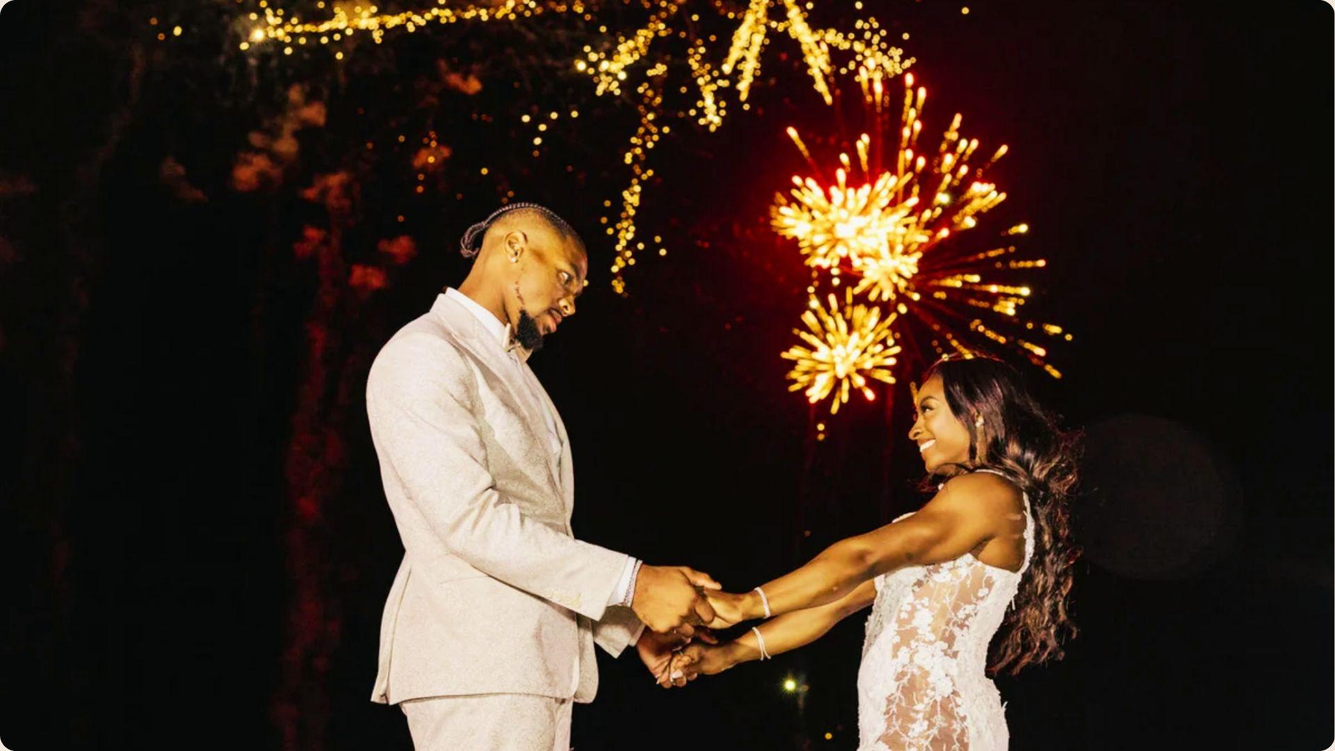 Simone Biles and Jonathan Owens share a dance at night with fireworks overhead.